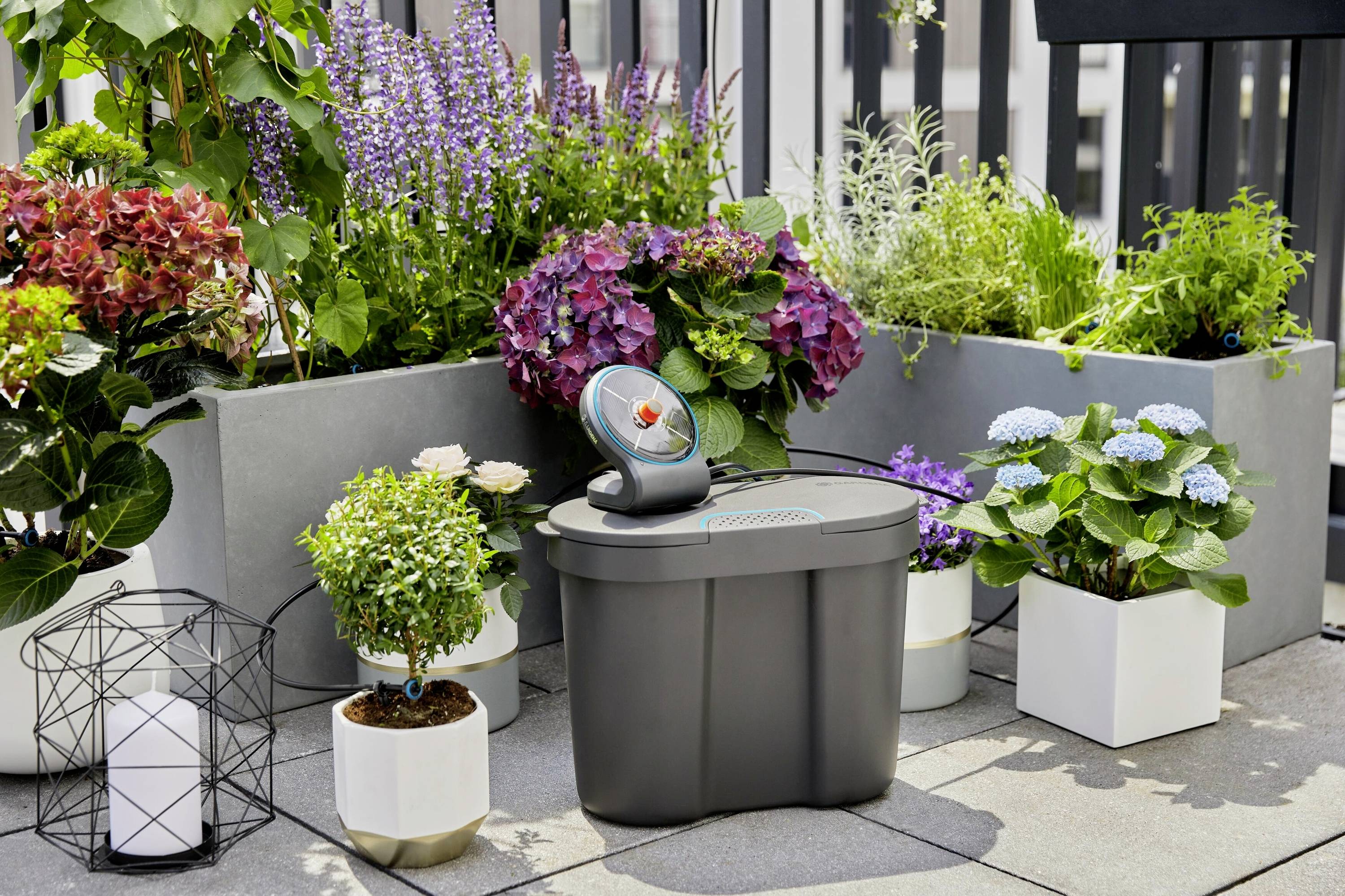 Ett automatiskt bevattningssystem på en terrass, omgivet av blommande växter i moderna planteringskärl.