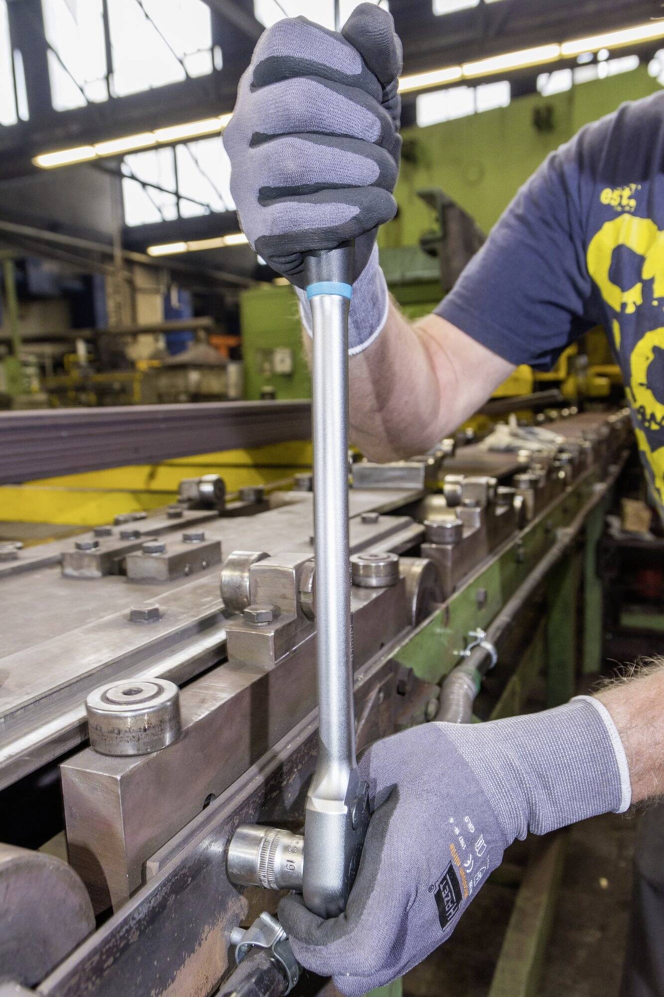 En person med arbetshandskar drar åt en skruv med en momentnyckel på en industriell maskin i en verkstad.