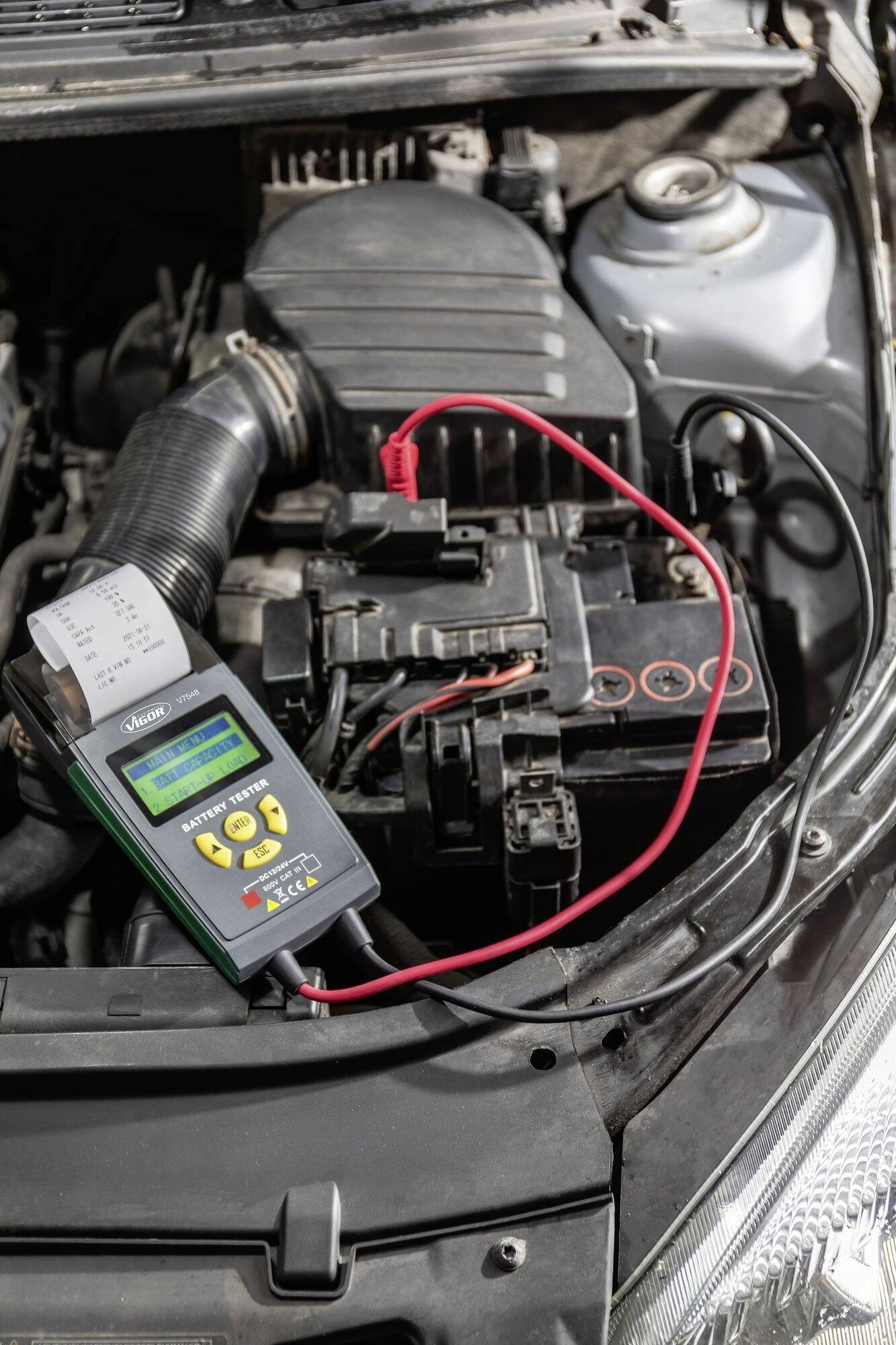 En bilbatteri testas med en digital batteritestare. Enheten visar resultatet på en liten skärm.