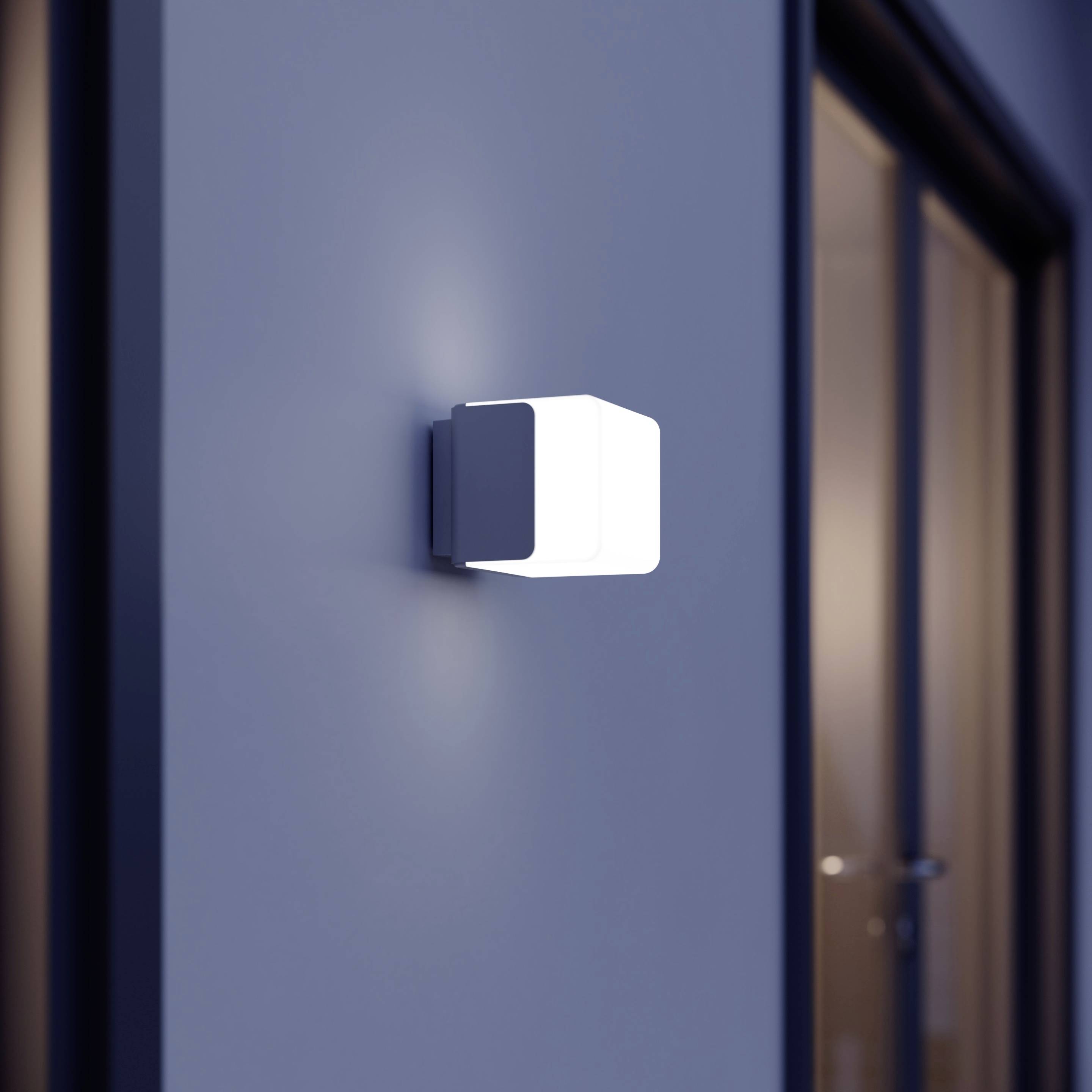 En modern utomhusvägglampa sprider mjukt ljus och är installerad på en blå vägg bredvid en glasdörr.