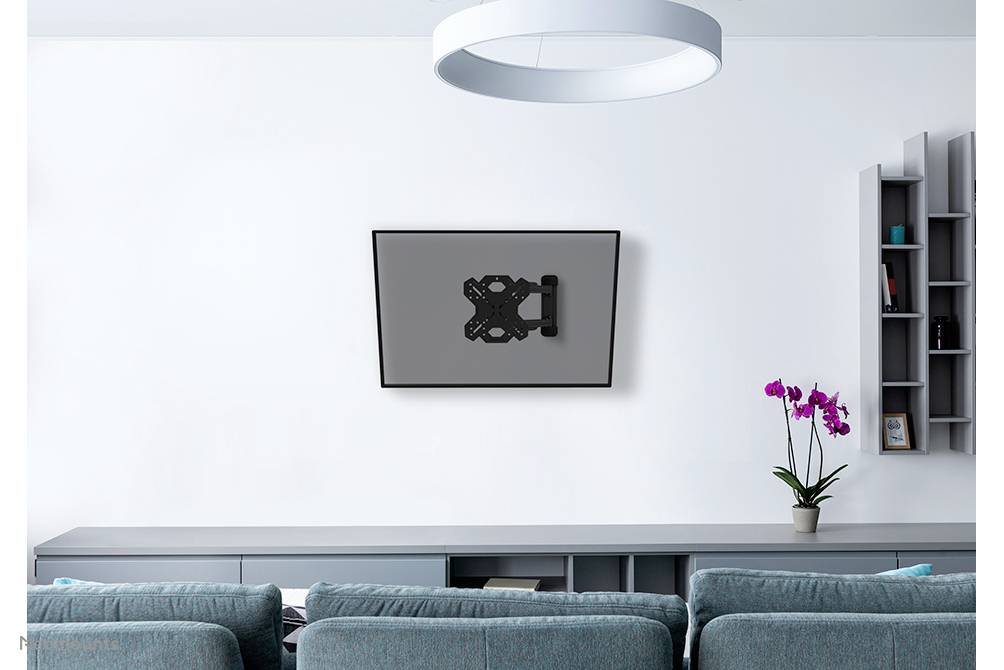 Vardagsrum med grå soffa, vägghylla, orkidé på byrå och väggmonterad TV-hållare utan TV på vit vägg.