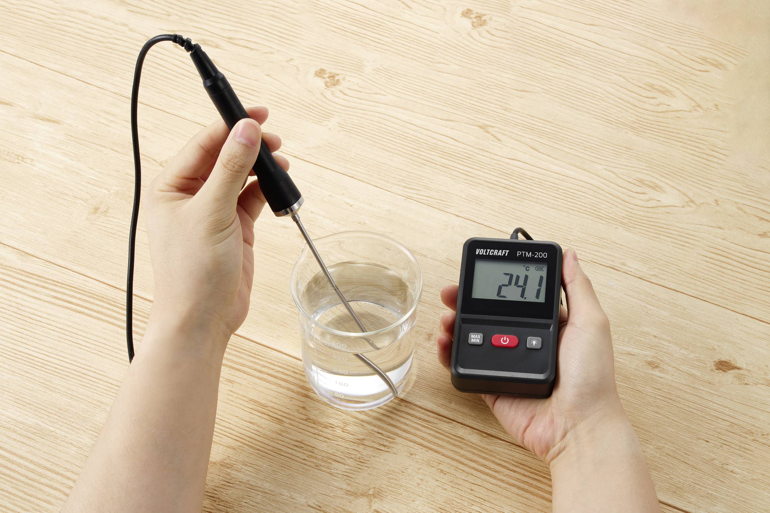 En person mäter vattentemperaturen i ett glas med en digital termometer som visar 24,1 grader.