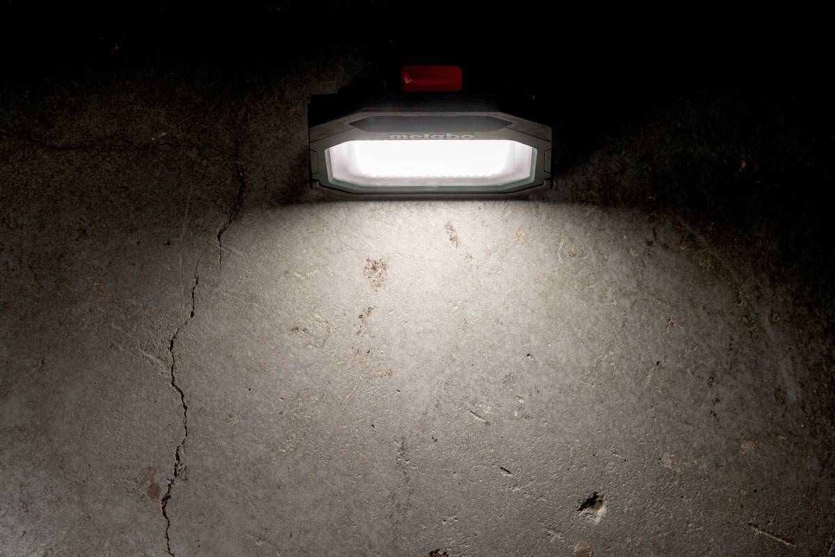 Bärbar lampa kastar ljus på mörkt betonggolv. En röd strömbrytare syns på lampan.