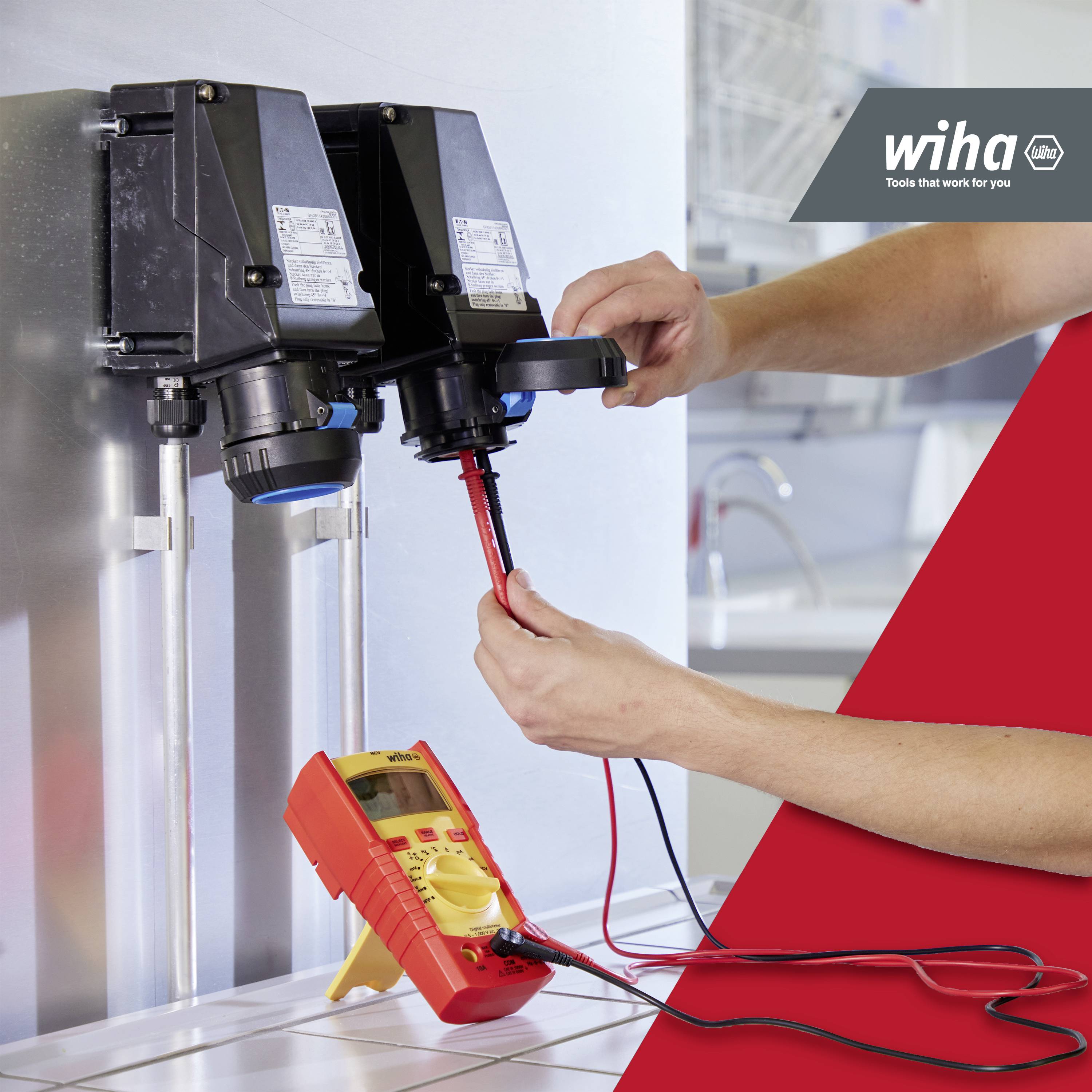 En person använder ett multimeter för att kontrollera elektriska anslutningar på två enheter. Längst upp till höger finns logotypen för ett hantverksföretag.