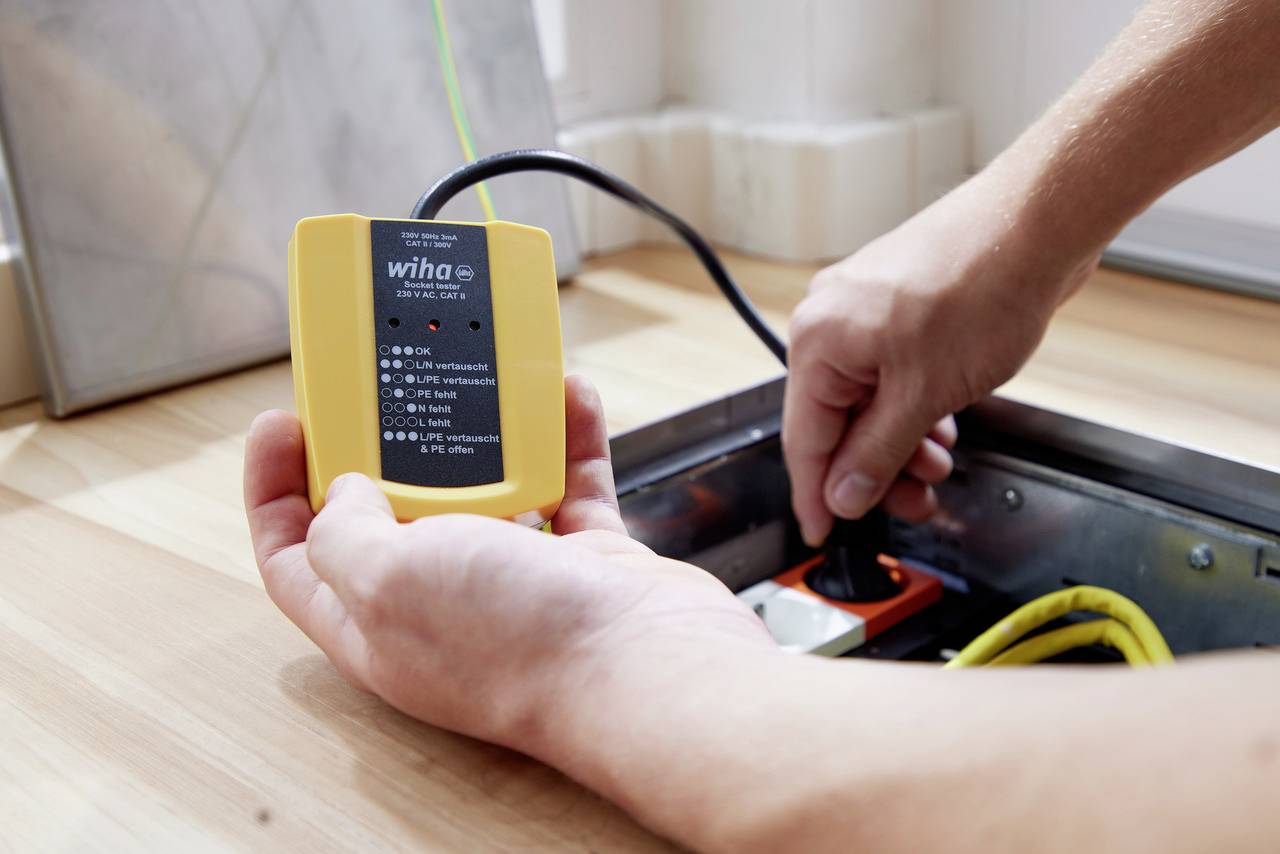 En person testar ett eluttag med ett gult Wiha-mätinstrument för spänningstestning.
