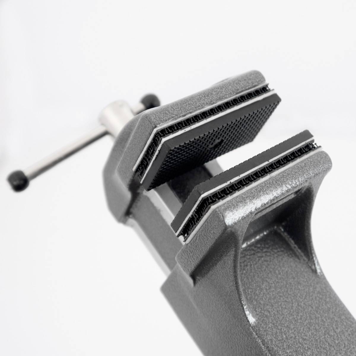 En grå metallarbetsbänkskruvtving med ett handtag på baksidan, öppen för att hålla ett föremål. Mot vit bakgrund.