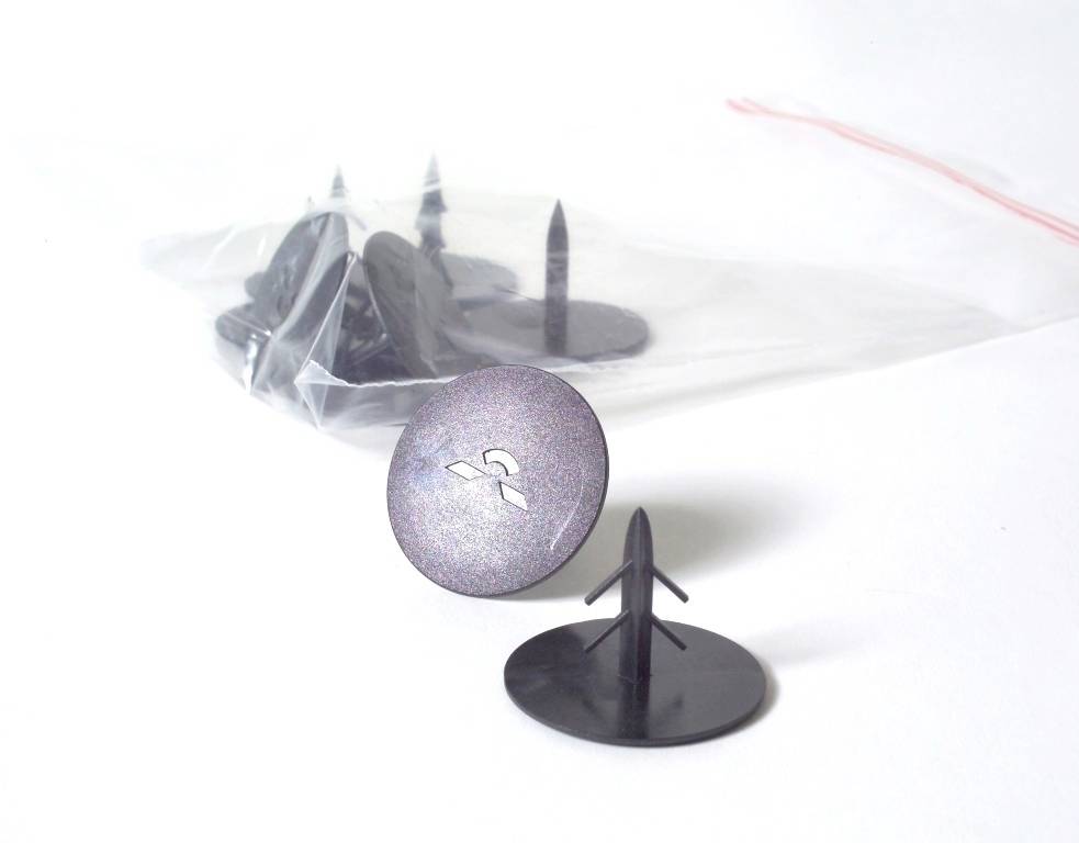 Plastnittar för fästning, svarta, med rund huvud. En påse i bakgrunden innehåller fler nitar.