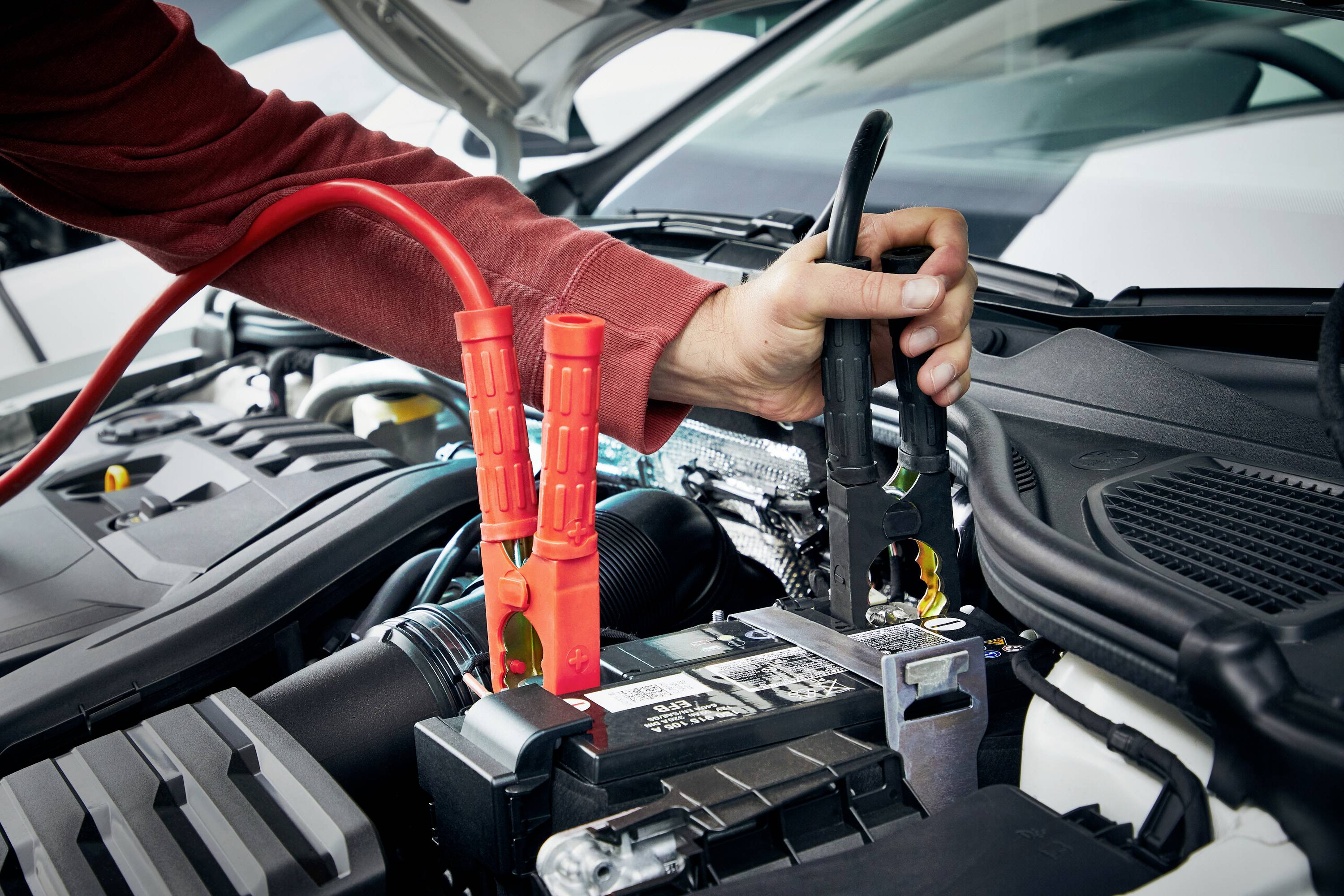 En bil får starthjälp med startkablar. En hand håller kabeln mot batteriet medan motorhuven är öppen.
