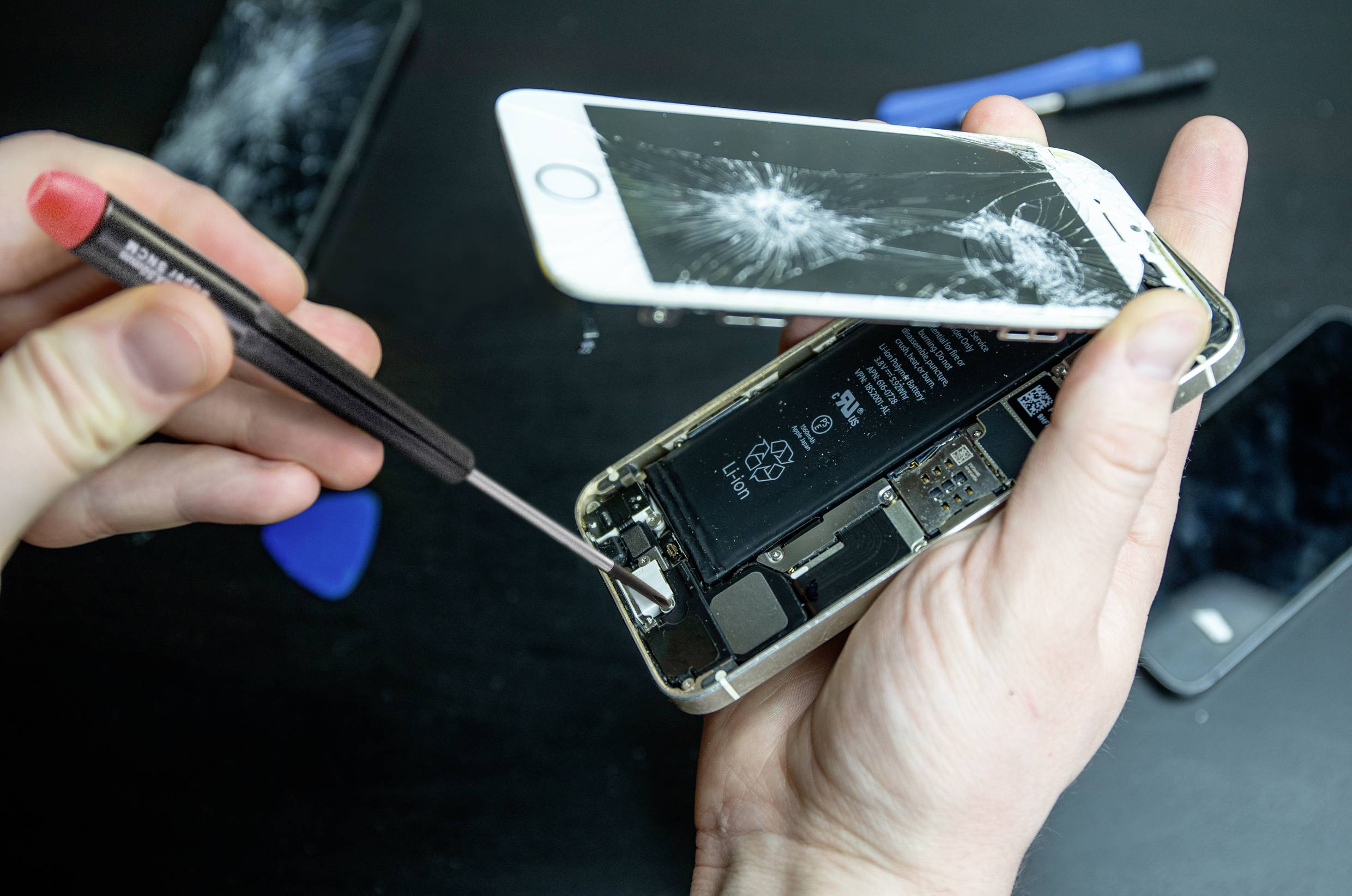 En person håller en smartphone med en sprucken skärm, öppnar den med verktyg för att visa dess inre komponenter. En reparationsscen.