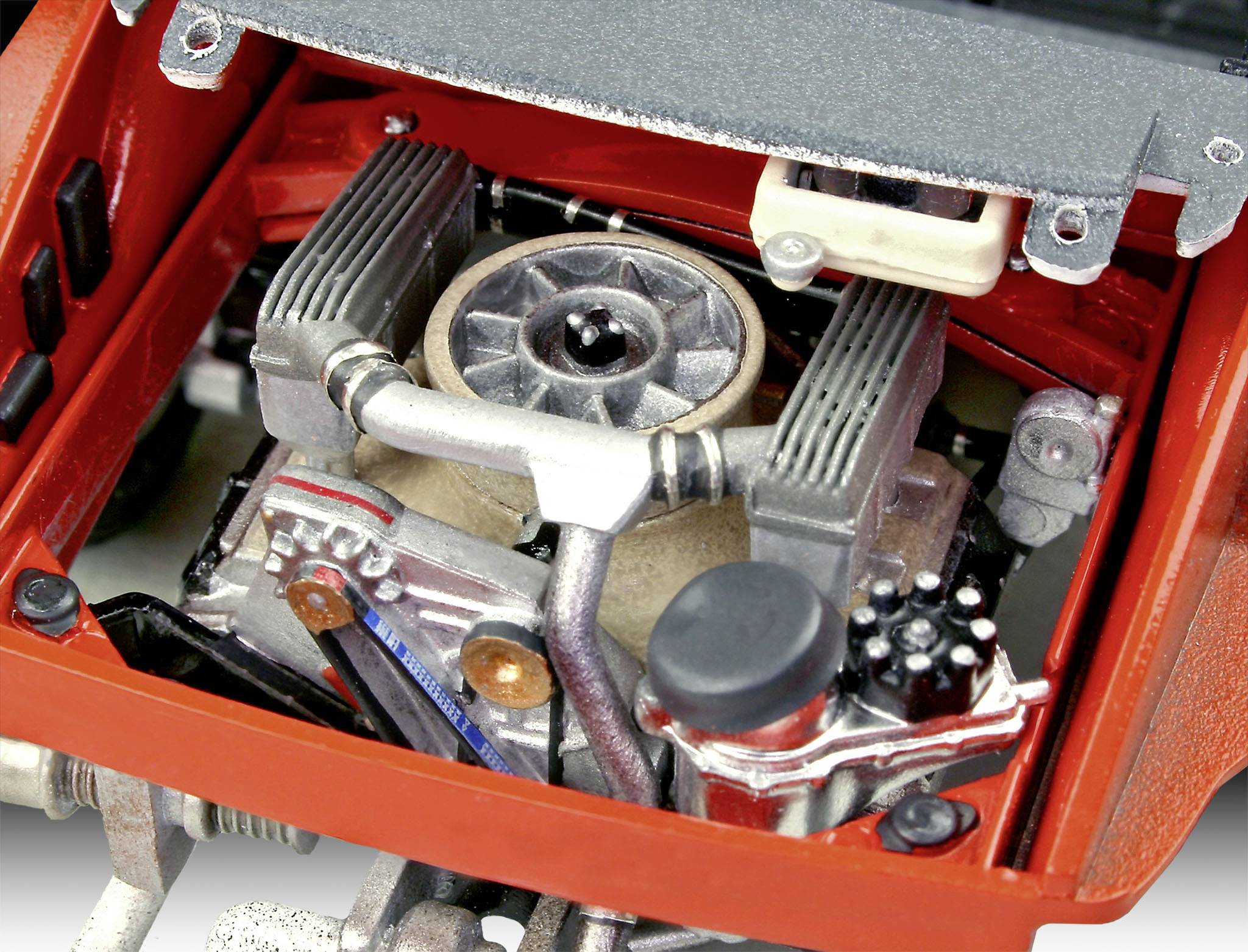 En motordetalj hos ett fordon med synlig fläkt och cylindrar, omgiven av röda karosseridelar. Den visar komplexa maskindetaljer.