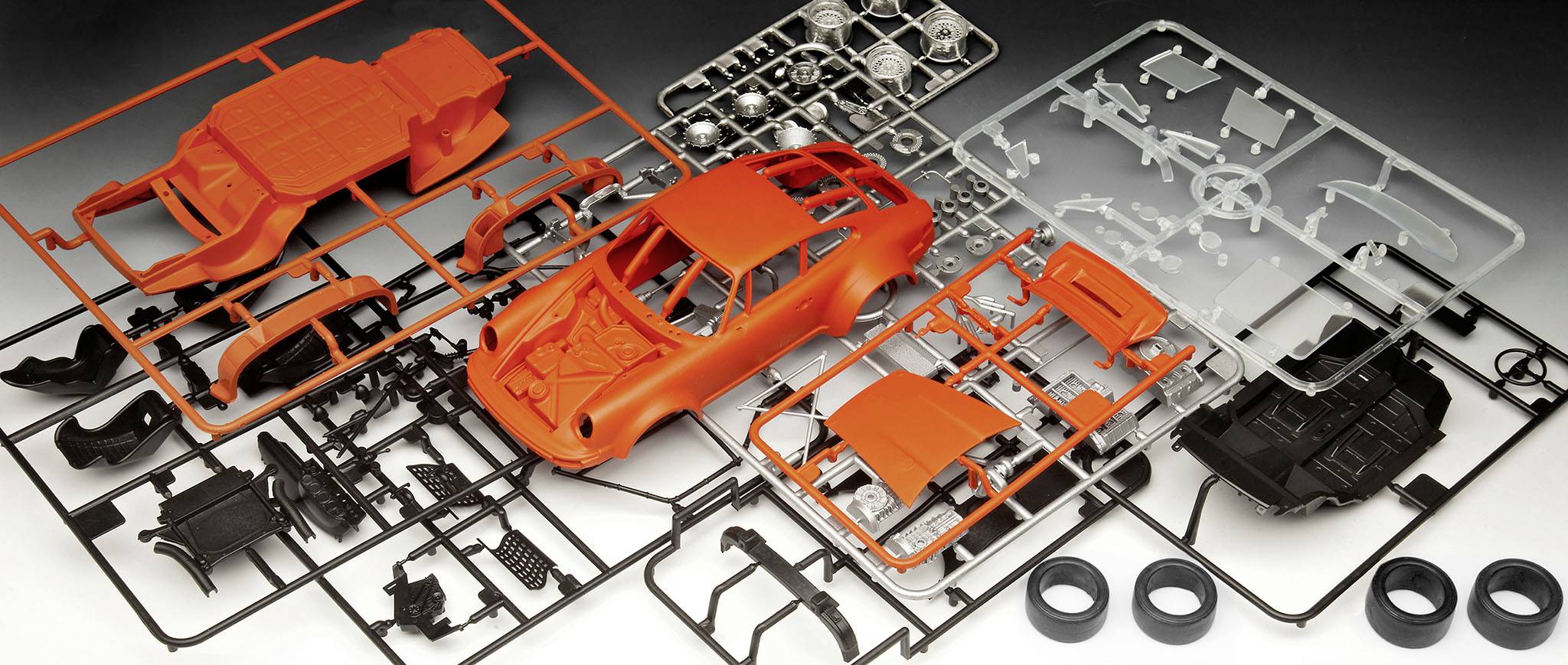 En modellbilsbyggsats med röda karosseridelar, svarta och grå komponenter samt fyra gummihjul, arrangerade på ett bord.