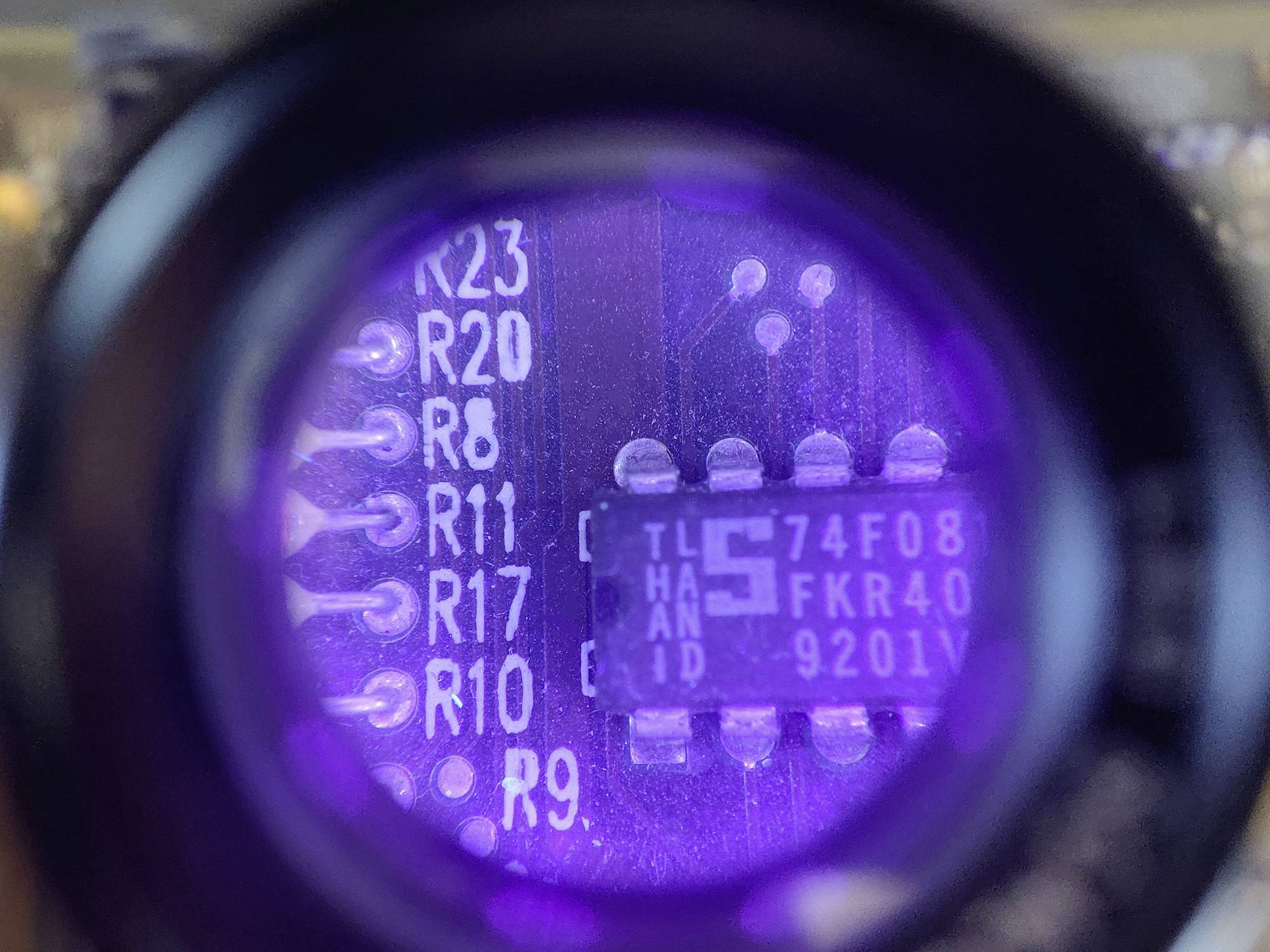 Närbild av ett kretskort med en mikrochip och lödpunkter; chipen är belyst under lila ljus och visar PIN-beteckningar.