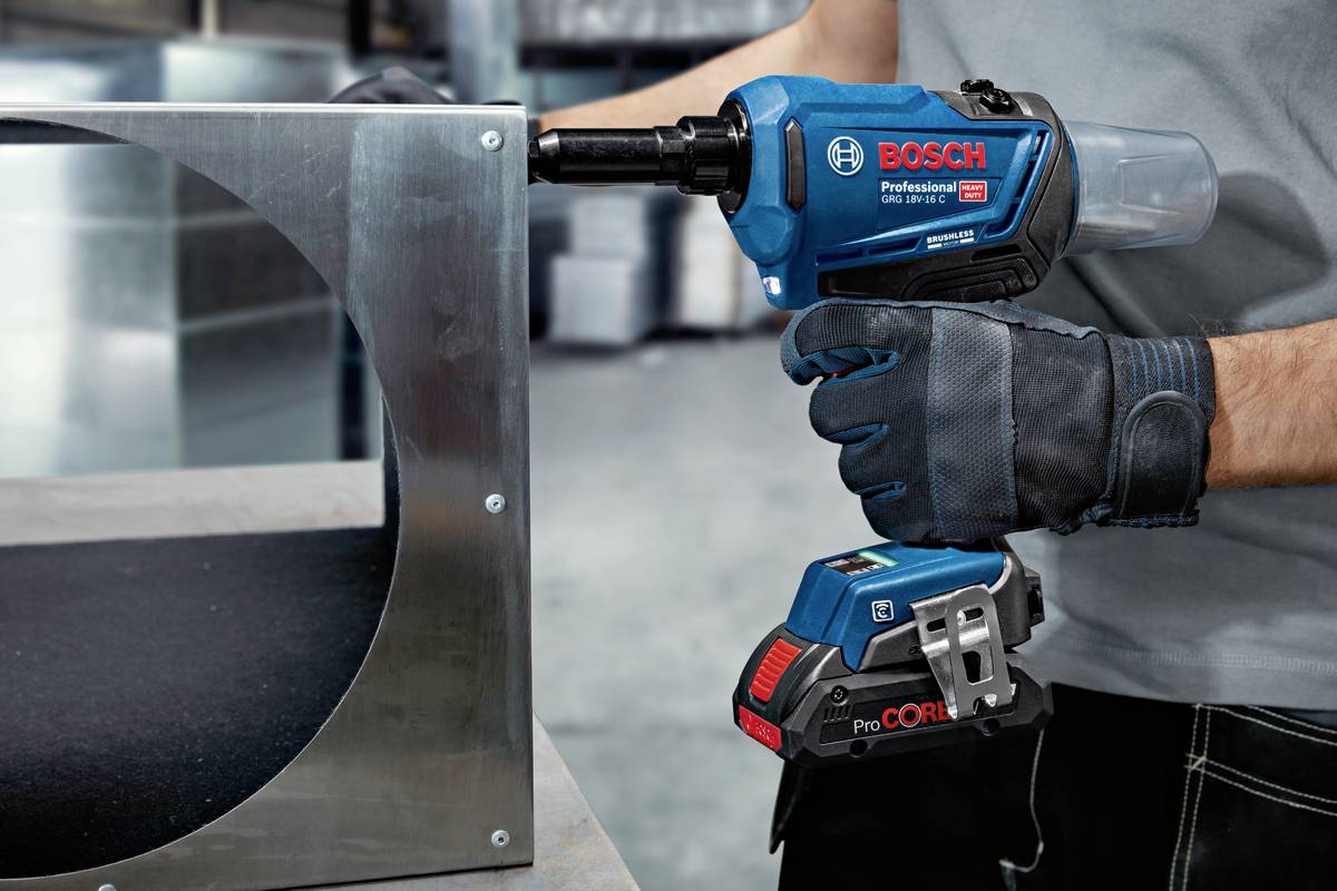 En person håller ett elektriskt verktyg från Bosch för att montera metall. Rummet i bakgrunden har en industriell design.