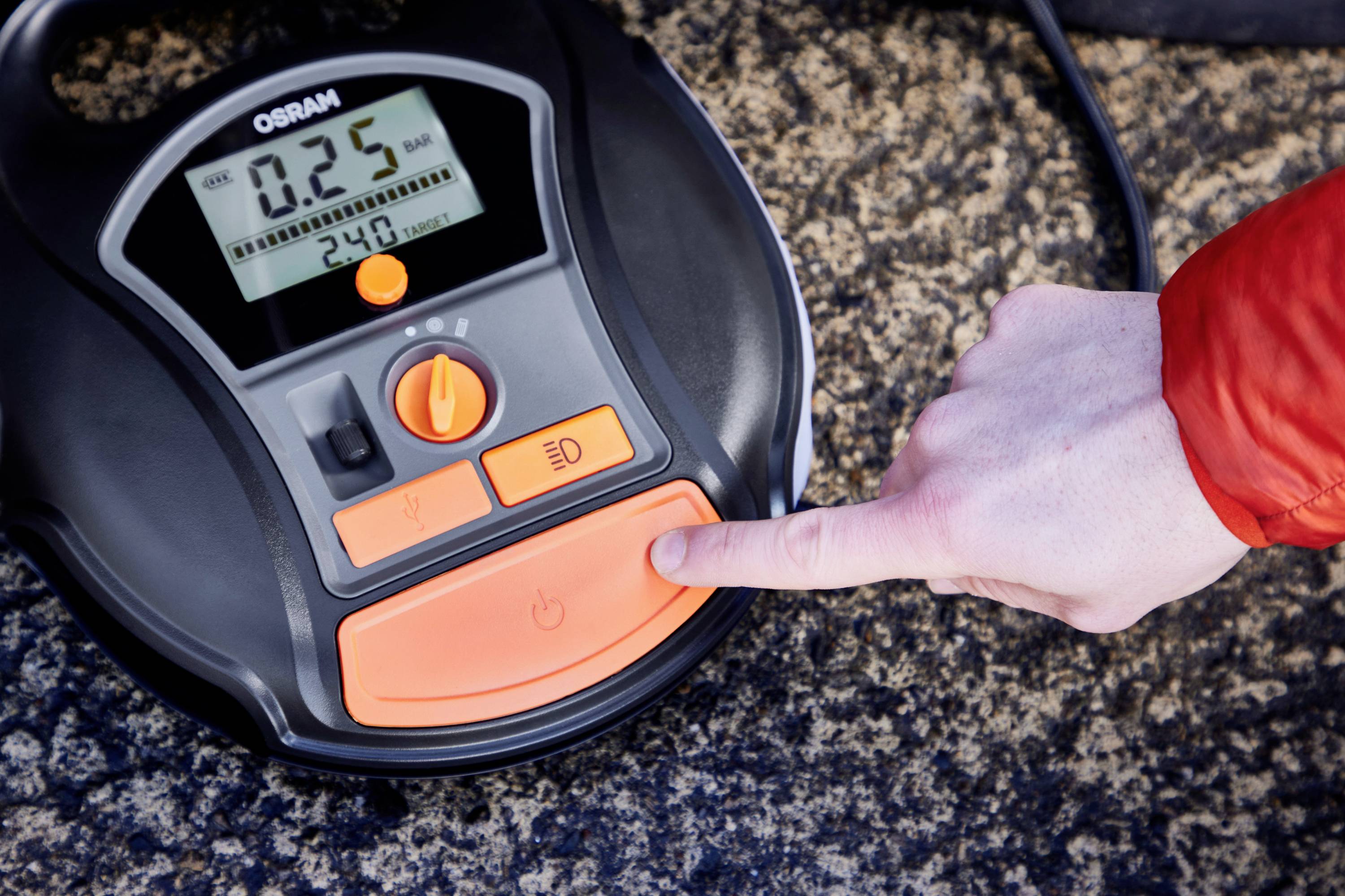 En hand trycker på en knapp på en digital däcktrycksmätare från OSRAM. Skärmen visar '0.25' bar.