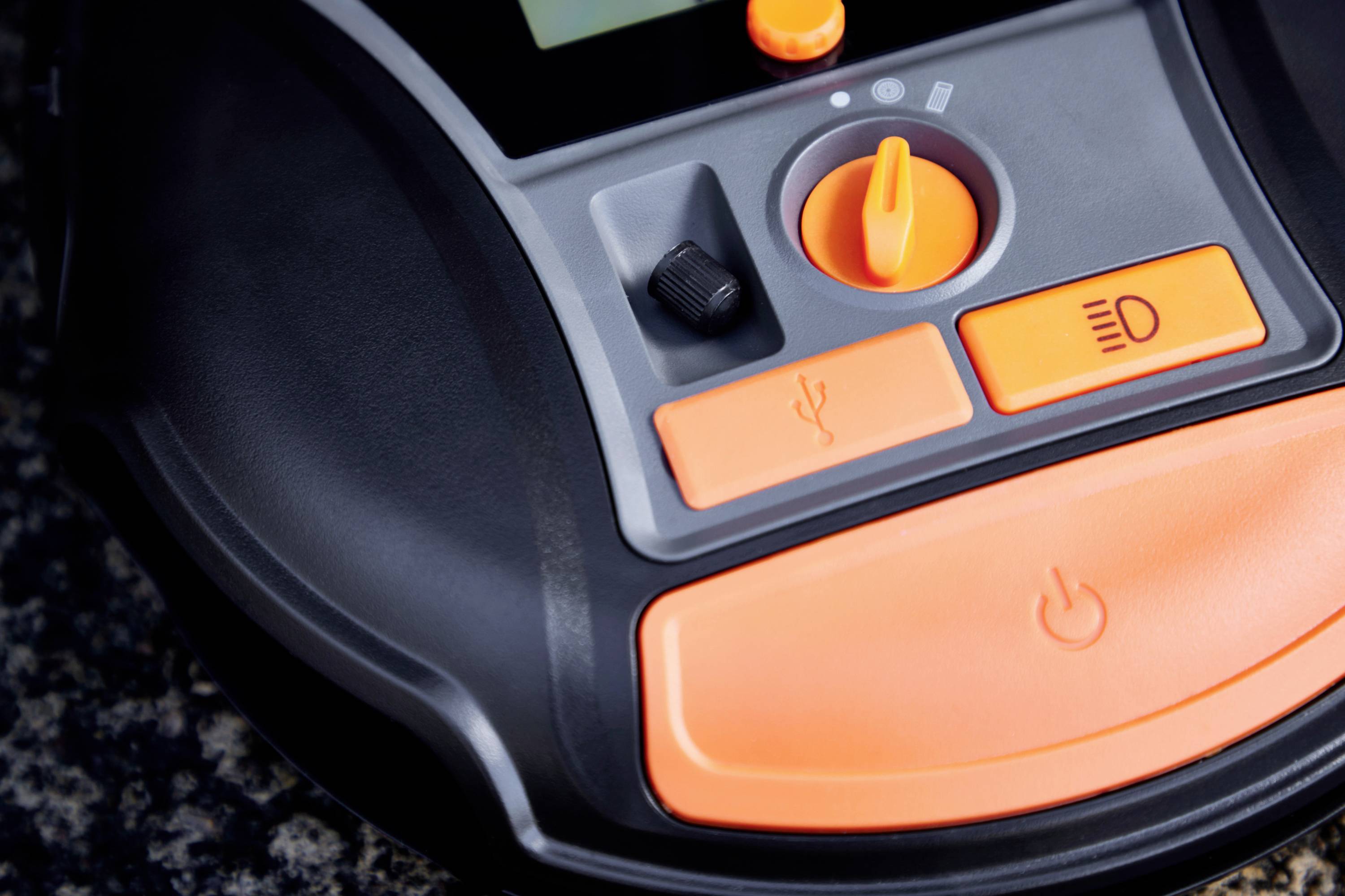 En närbild av en elektronisk kontrollpanel med orangefärgade knappar och en vridomkopplare, sannolikt en del av en apparat.