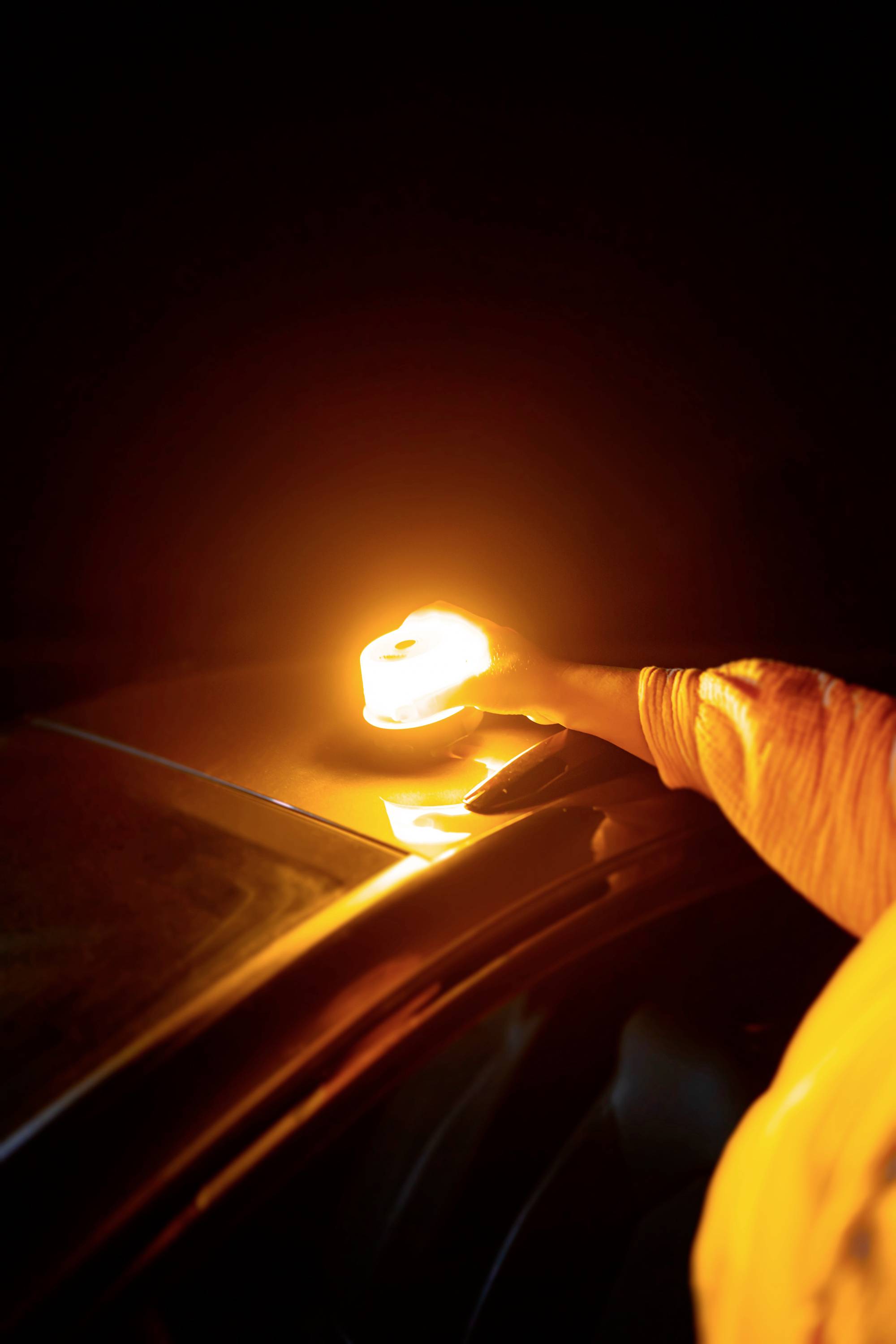 En hand placerar ett lysande orange ljus på taket på en bil i mörkret, möjligen som en varningssignal.