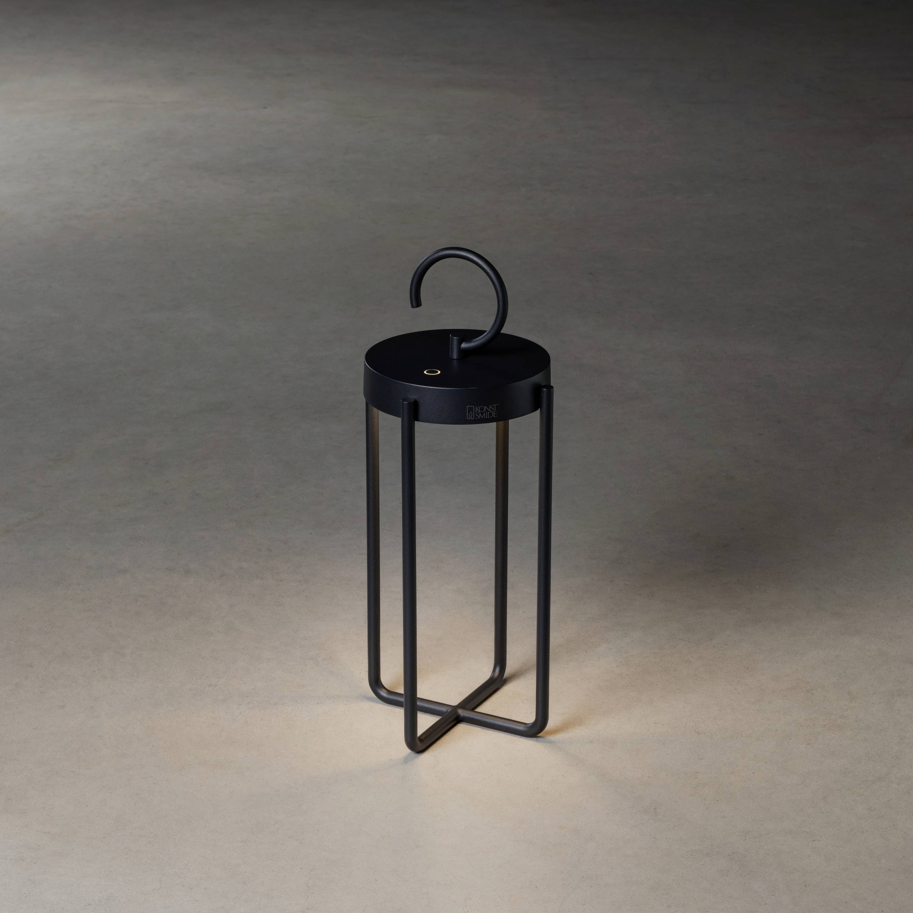 Mörk, modern lykta med elegant, böjt handtag. Står på grå yta. Perfekt för stilfull belysning inomhus.