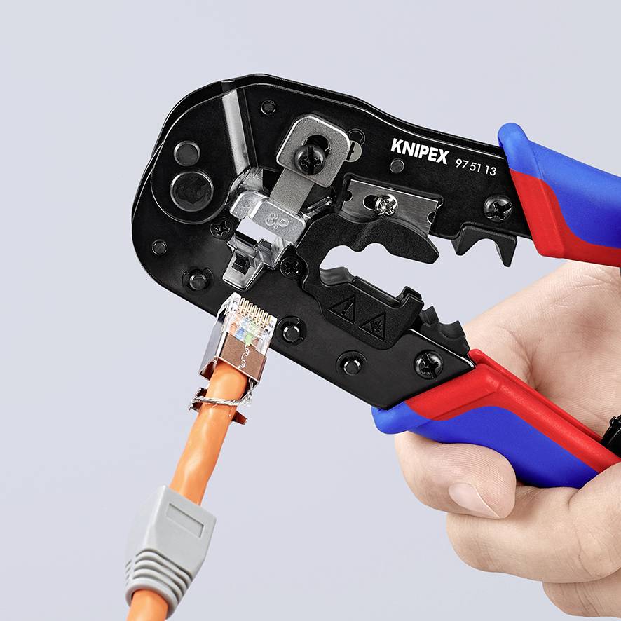 En hand håller ett KNIPEX-verktyg som crimpar en orangefärgad kabel. Kabelanslutningar och verktygsdetaljer syns.