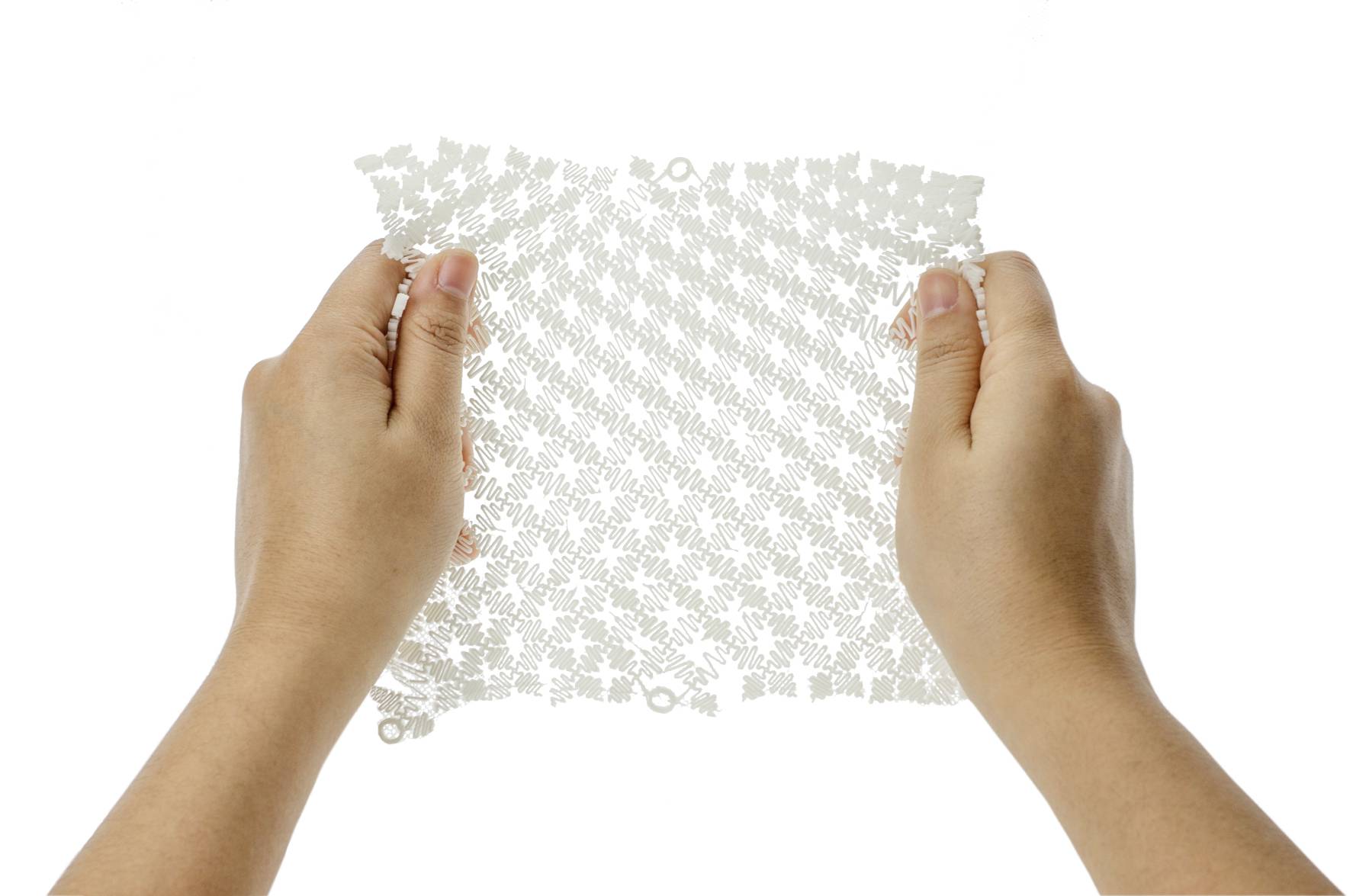 Två händer håller ett flexibelt, transparent material med ett rombformat mönster på vit bakgrund.