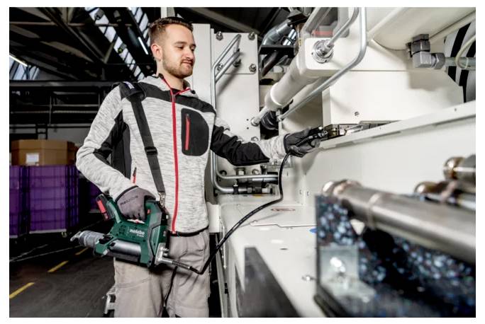 En arbetare i skyddsutrustning inspekterar och manövrerar maskineri i en industriell anläggning, medan han håller en elektrodriller bredvid stora rör och utrustning.