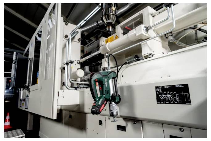 Industriell maskin med en grön trådlös borrmaskin fäst vid ett robotiserat spännfäste på en fabrikstillverkningslinje.