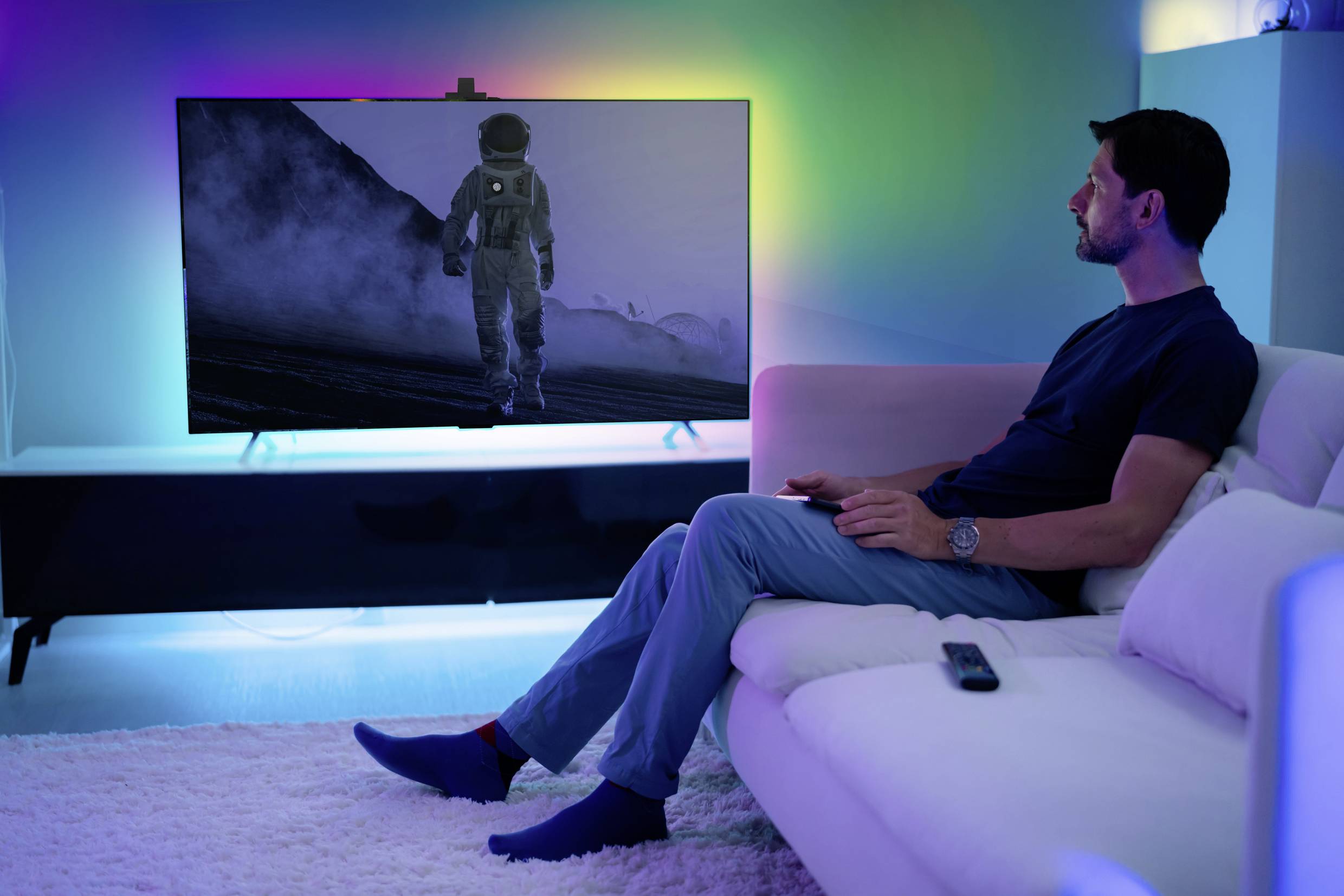 En man sitter på en soffa och tittar på en film på en stor skärm som visar en astronaut i en månlandskap.