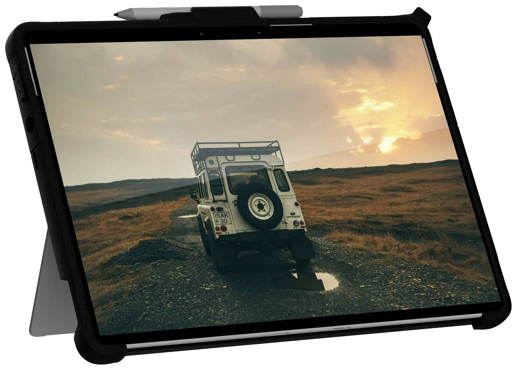 En surfplatta visar ett foto av en SUV på en smal väg i ett kargt landskap vid solnedgången.