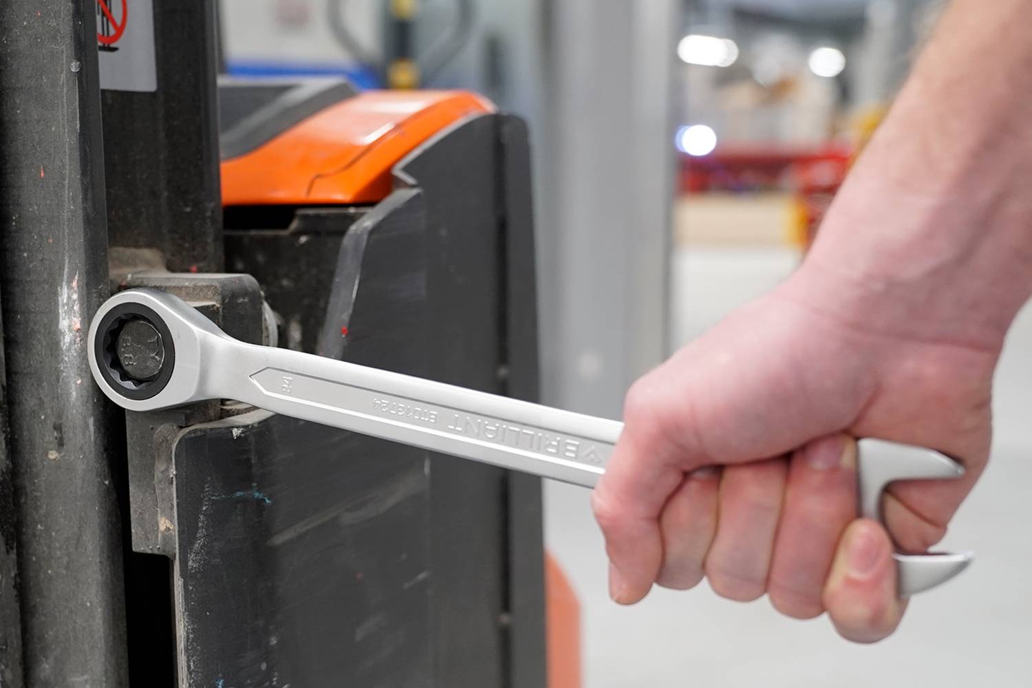 En hand håller en silverfärgad skiftnyckel som placeras mot en stor, svart metallenhet.