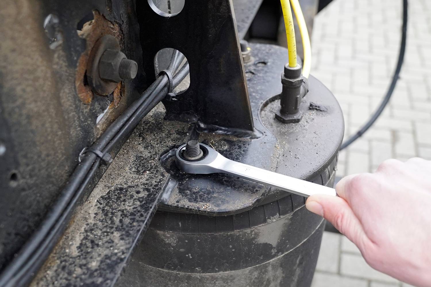 En person drar åt en mutter på en metalldetalj med en skiftnyckel. Kablar löper ovanför och är säkrade med en gul tråd.