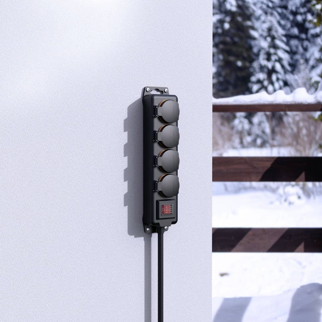 En grenuttag är monterad på en vägg. I bakgrunden syns ett snötäckt landskap med träd och ett staket.