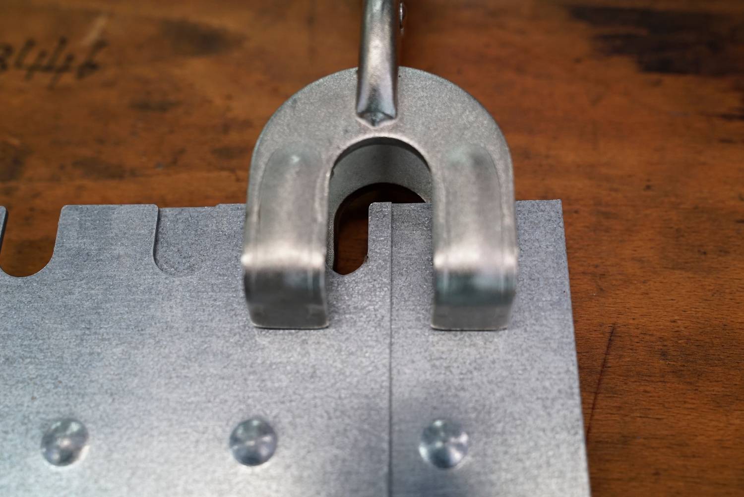 Metallåset griper över två sammanlänkade metalldelar på en träyta och symboliserar styrka och förbindelse.
