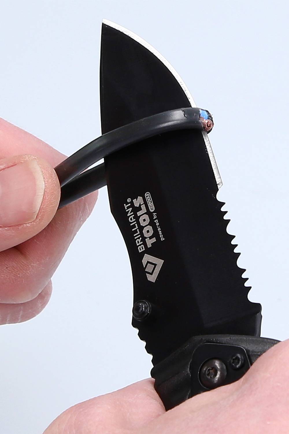 En hand håller en svart kniv och klipper av en kabel. Kniven har sågtandade kanter och texten 'Brilliant Tools' tryckt på sig.