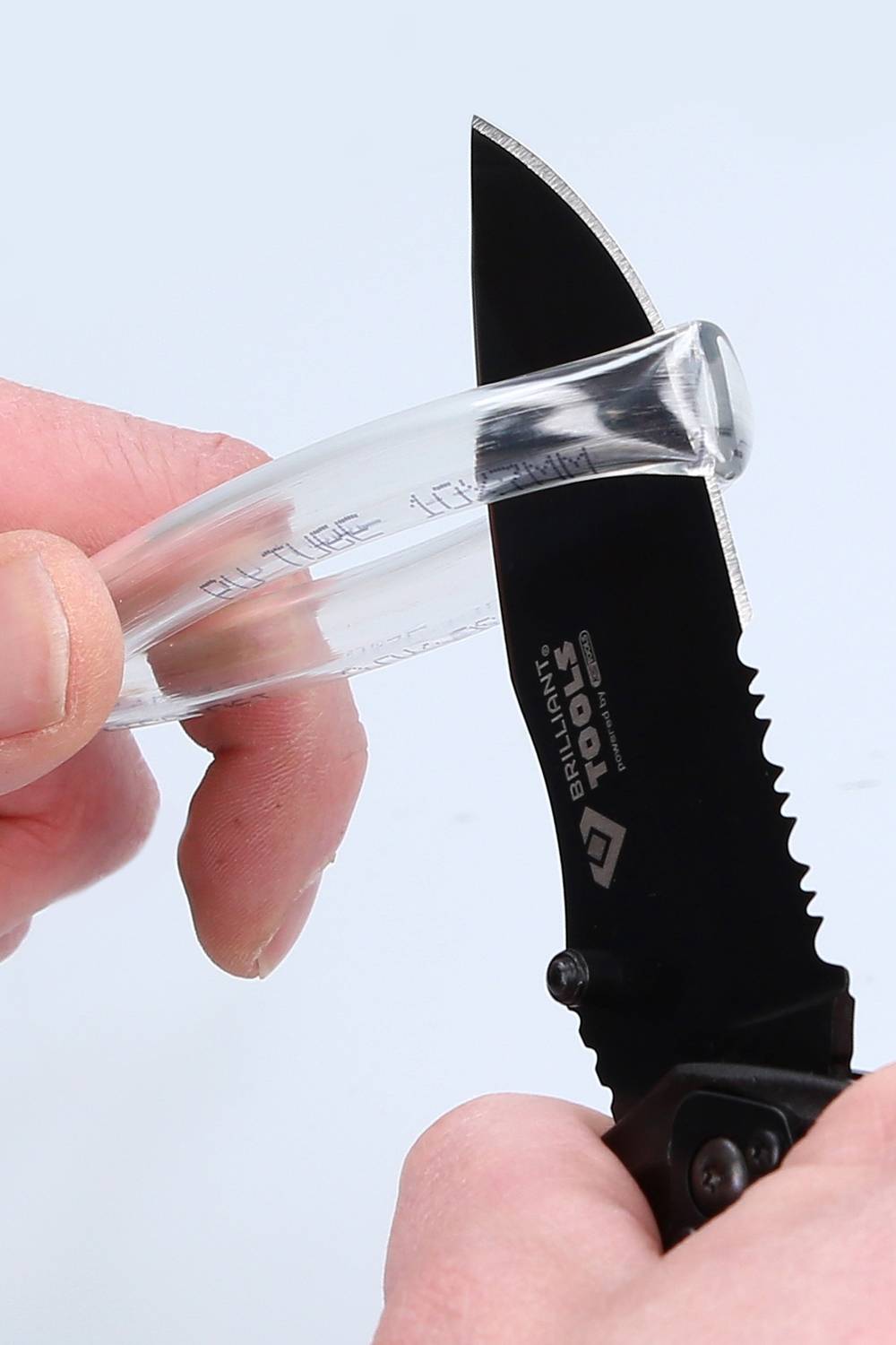 En hand håller ett genomskinligt plastföremål medan en annan hand skär det med en svart kniv.