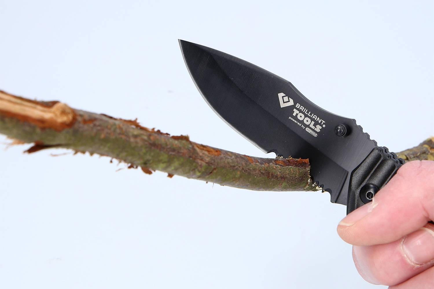 En hand håller en svart fällkniv och klipper av en gren.