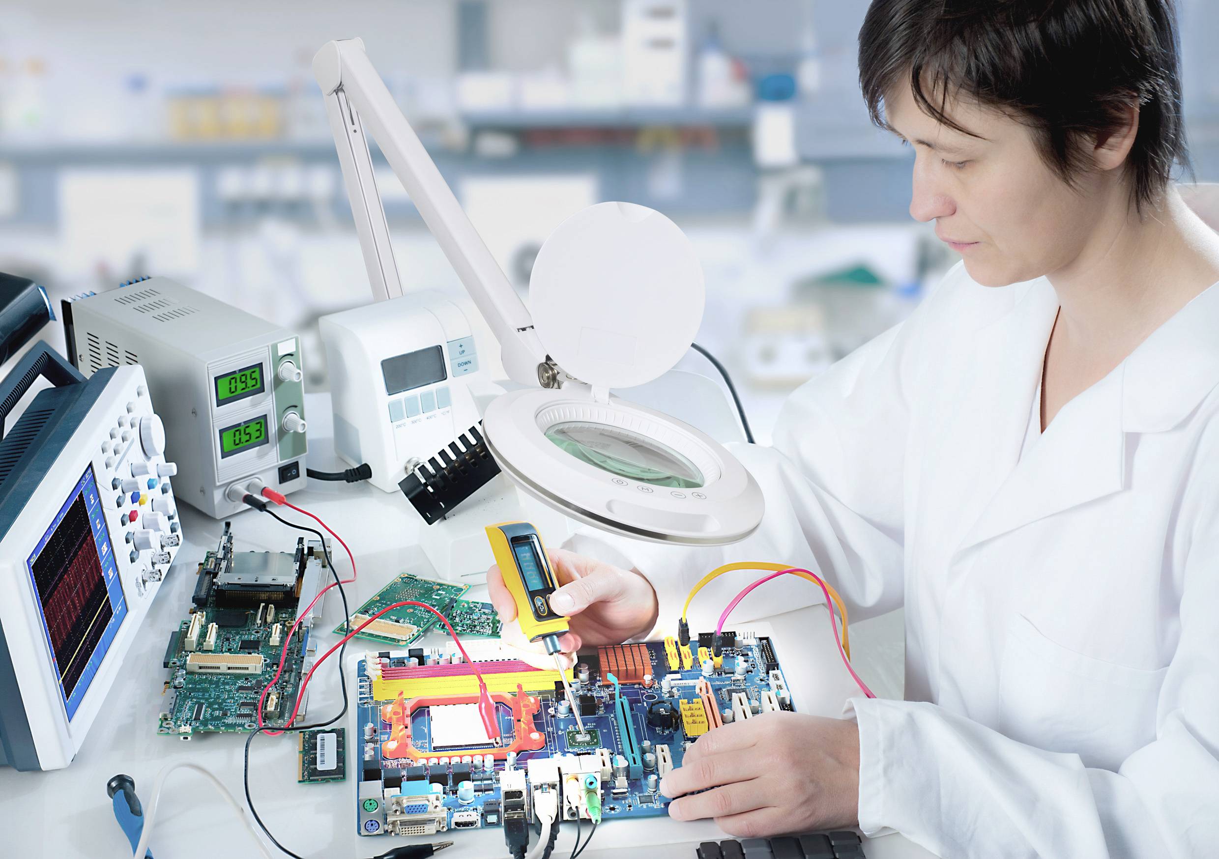 En person i ett laboratorium reparerar eller testar ett kretskort med olika mätinstrument, omgiven av teknisk utrustning.