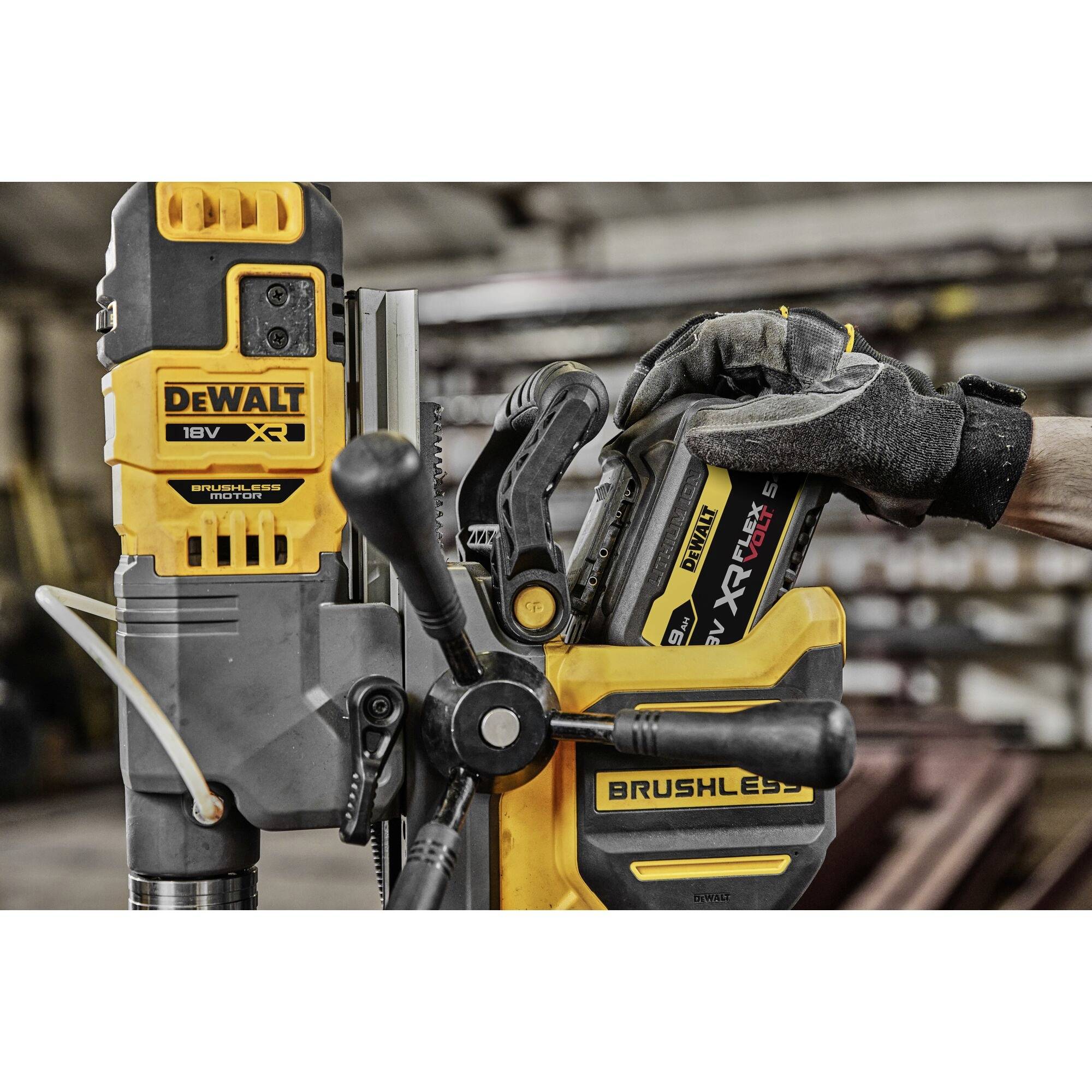 En person byter batteriet på ett gult, borstlöst DeWalt-elverktyg i en verkstadsmiljö.
