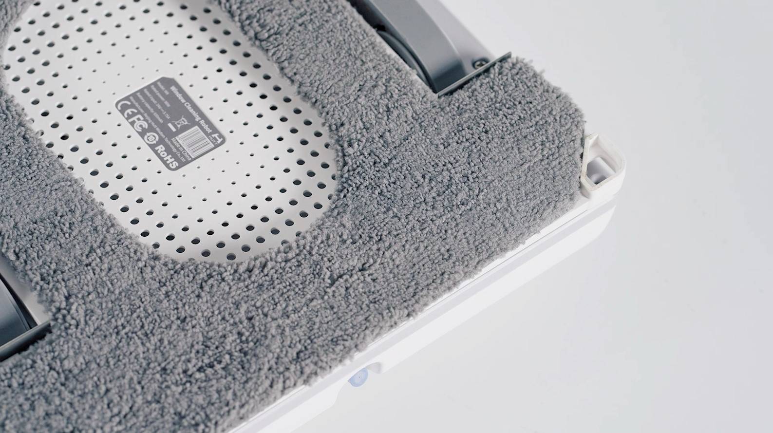 Dammsugarrobot detaljvy: En grå borste på undersidan, omgiven av ventilationsöppningar och en etikett med teknisk information.