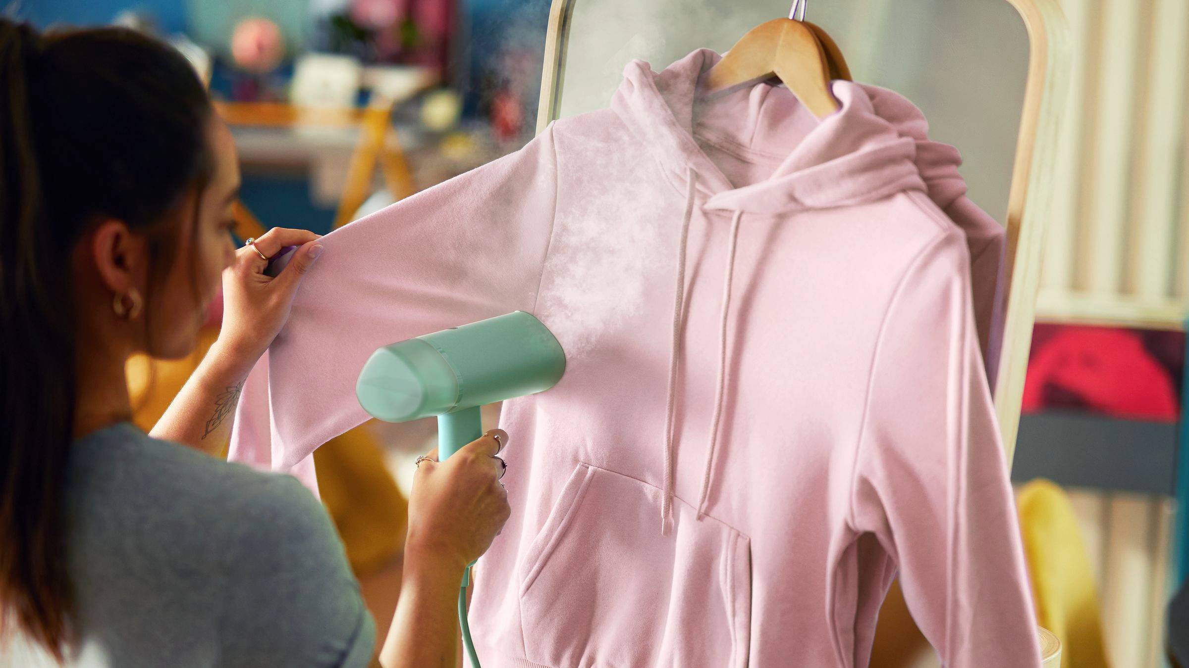 En personångar en rosa hoodie med en handhållen ångare framför en spegel.