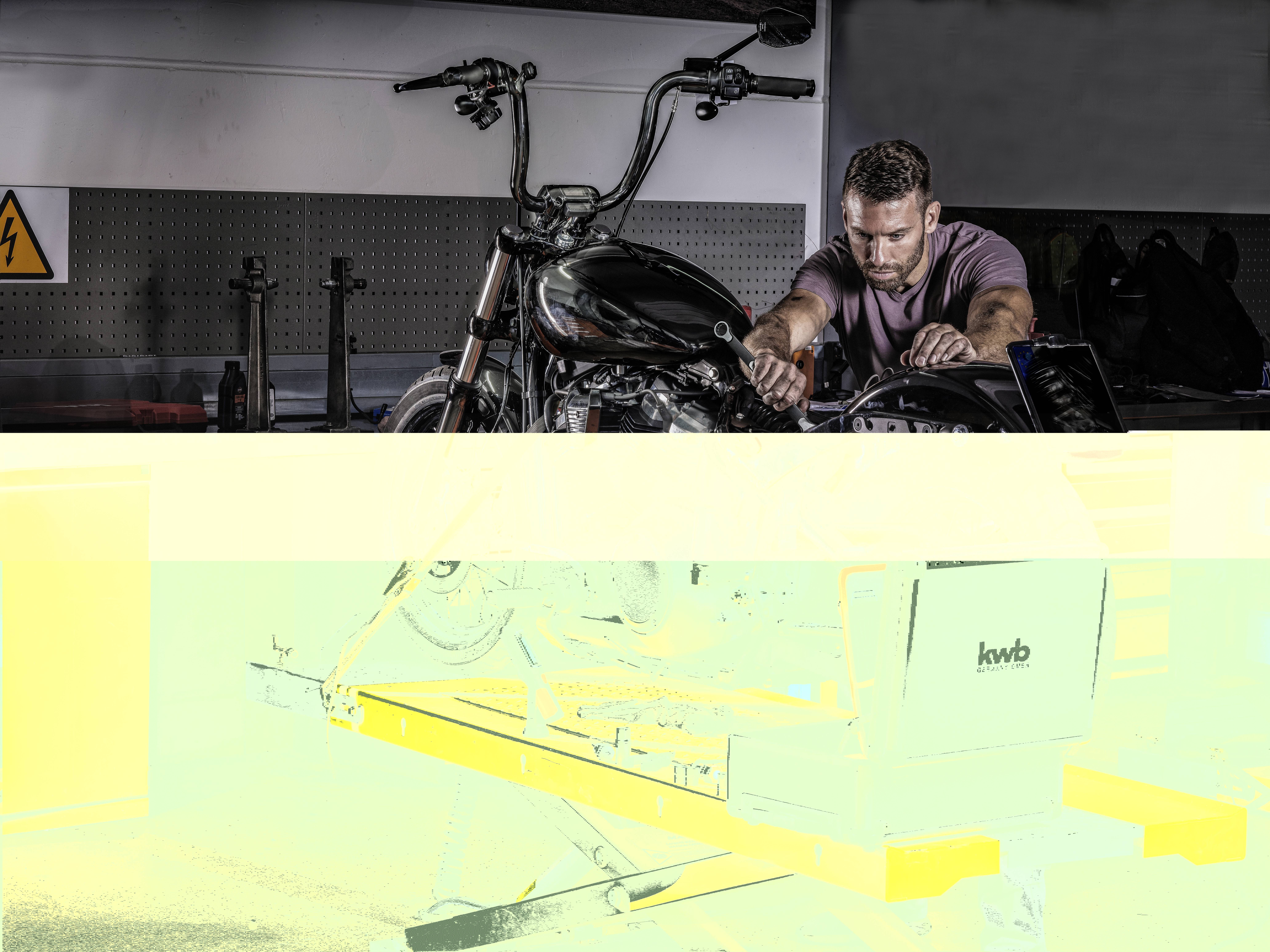 Man reparerar motorcykel i verkstad med skruvnyckel, koncentrerad i arbetet, i bakgrunden ytterligare verktyg.