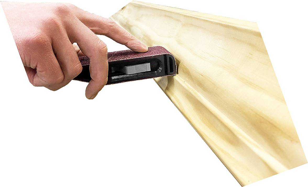 En hand håller ett slipverktyg och bearbetar kanten på ett trästycke.