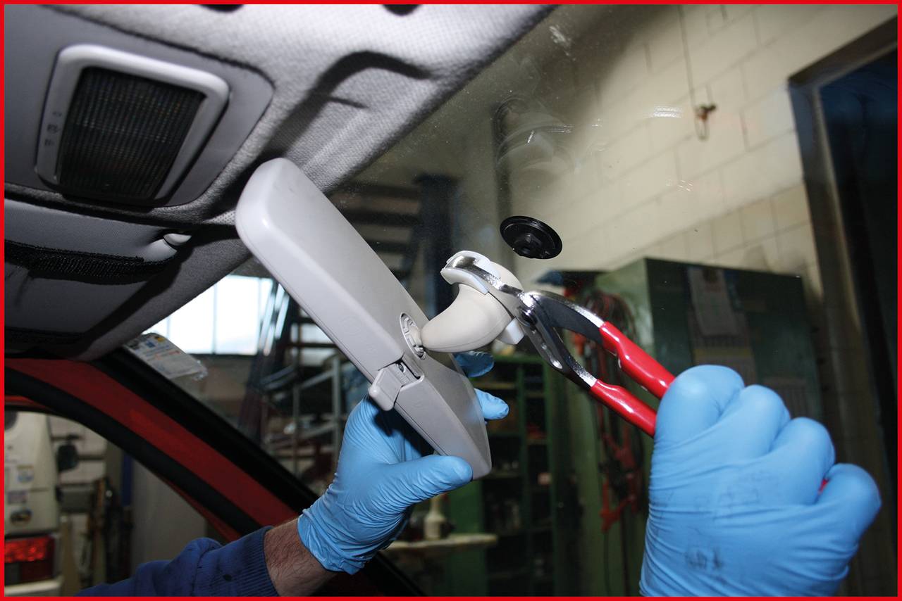 En person med blå handskar tar bort backspegeln från en bil med hjälp av en tång.