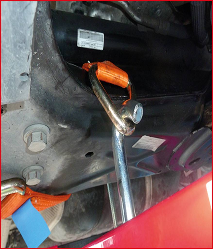 En bärgningskrok är fäst vid en bil. Ett orangefärgat spännband är också synligt, som säkrar strukturen.