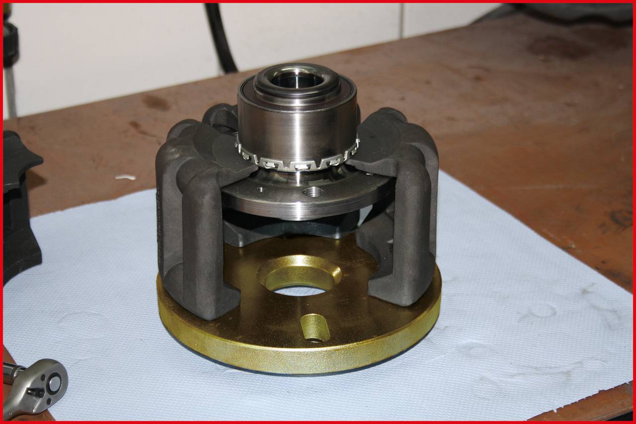 En maskindel med metalliska och mekaniska komponenter ligger på en arbetsbänk. Den har en central cylinderformad struktur.