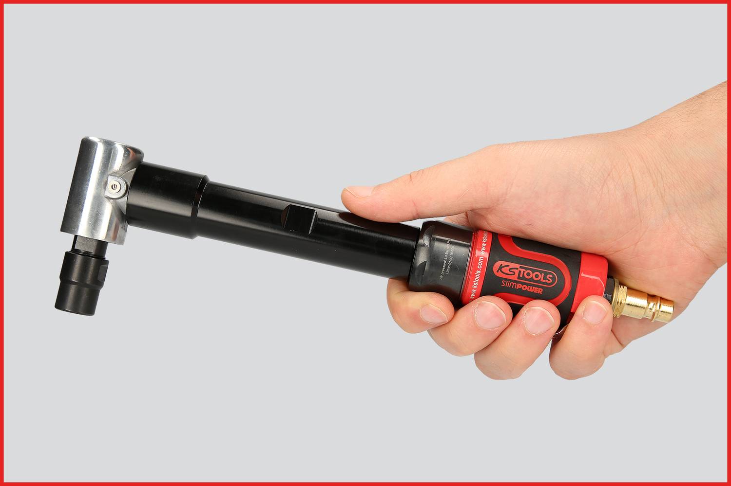 En hand håller ett rött och svart verktyg med metallhuvud och slangkoppling, sannolikt ett tryckluftsverktyg.