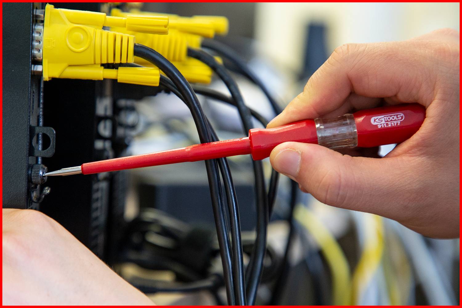 En hand håller en röd skruvmejsel och drar åt en skruv på en nätverksenhet. Gula kablar är anslutna ovanpå.