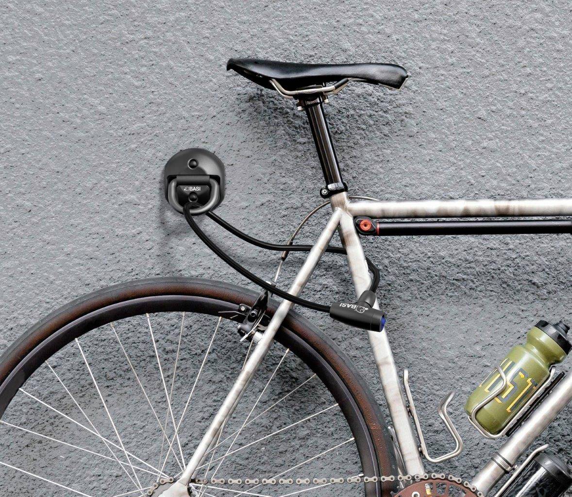 En cykel med en flaskhållare och ett lås är säkrad vid en grå vägg.