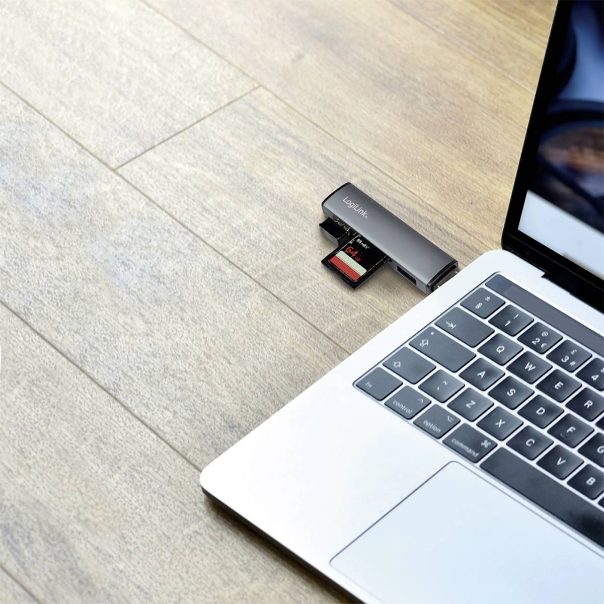 En laptop på ett träbord, bredvid ett USB-minne och ett SD-kort. Laptopskärmen visar en suddig display.
