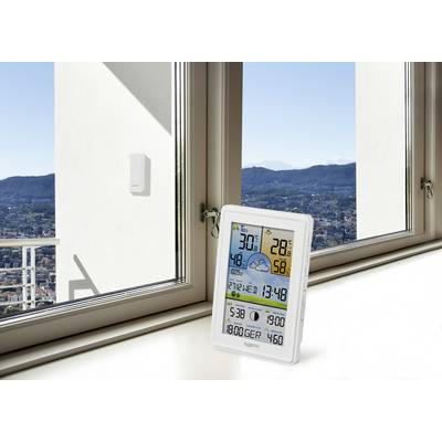 En digital väderstation på en fönsterbräda visar temperatur, luftfuktighet, tid och väderprognos. Bakgrund: utsikt över staden.