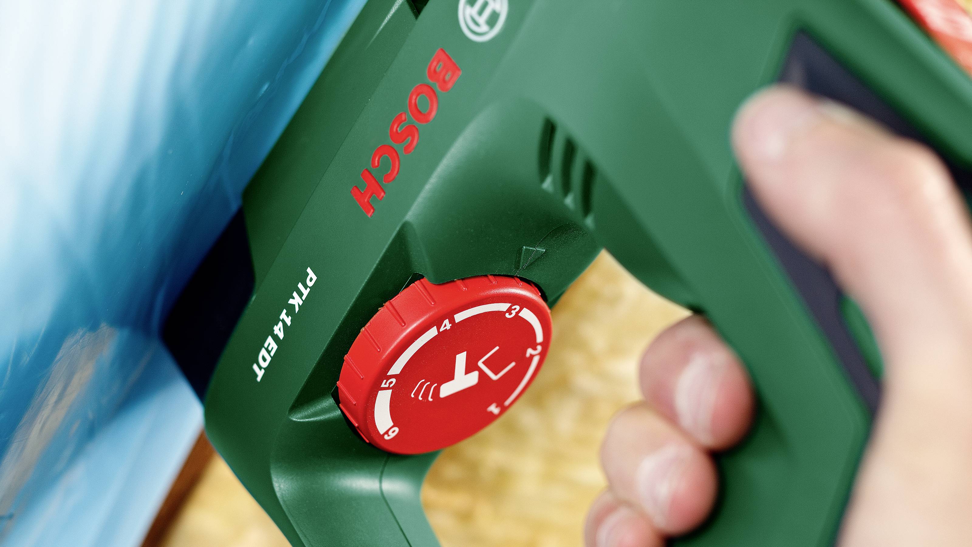 En person håller en grön Bosch-häftpistol, redo att användas. Den röda inställningsratten är synlig.