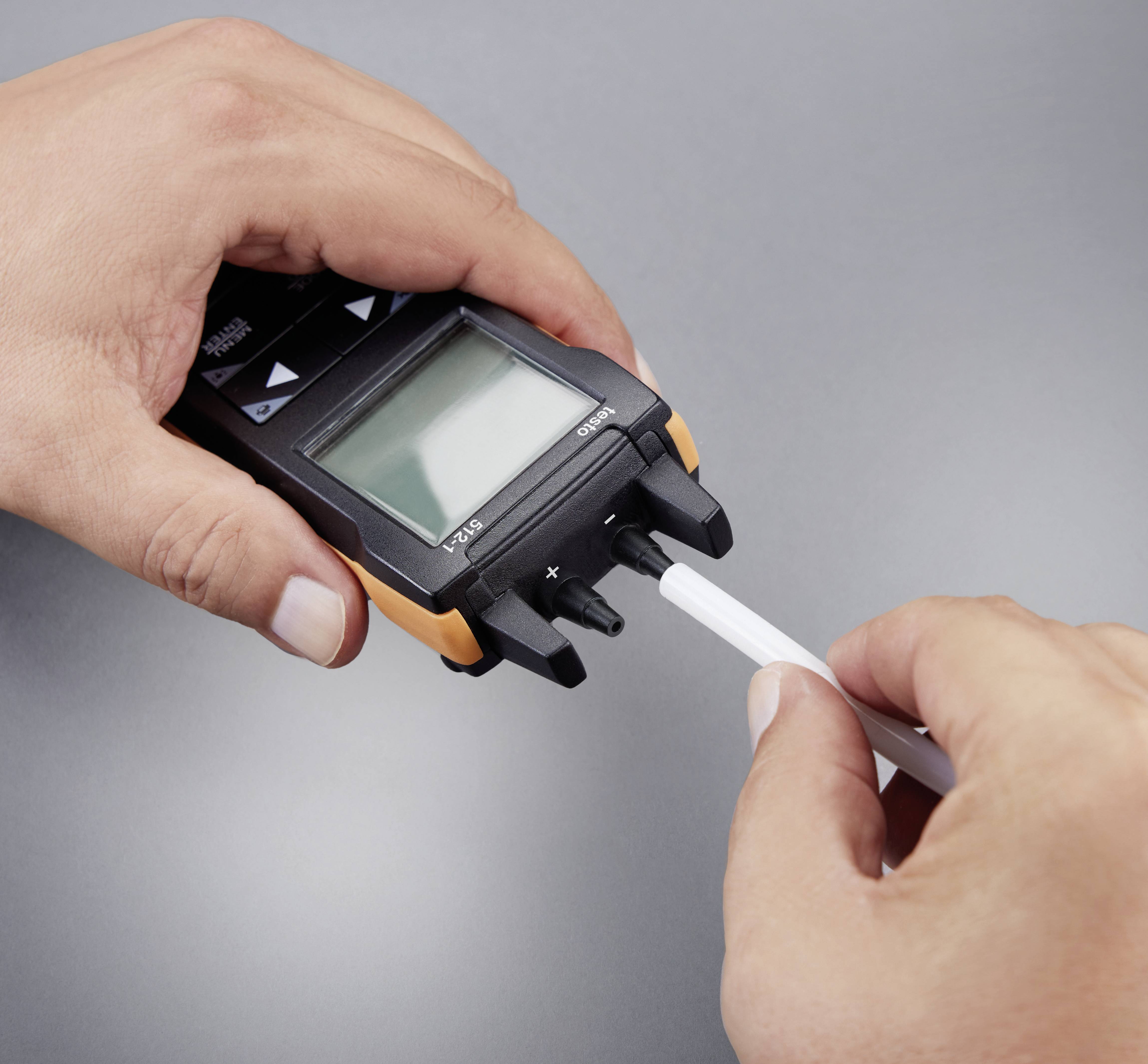 En person håller en digital mätapparat i vänster hand medan höger hand ansluter en sensor till enheten.